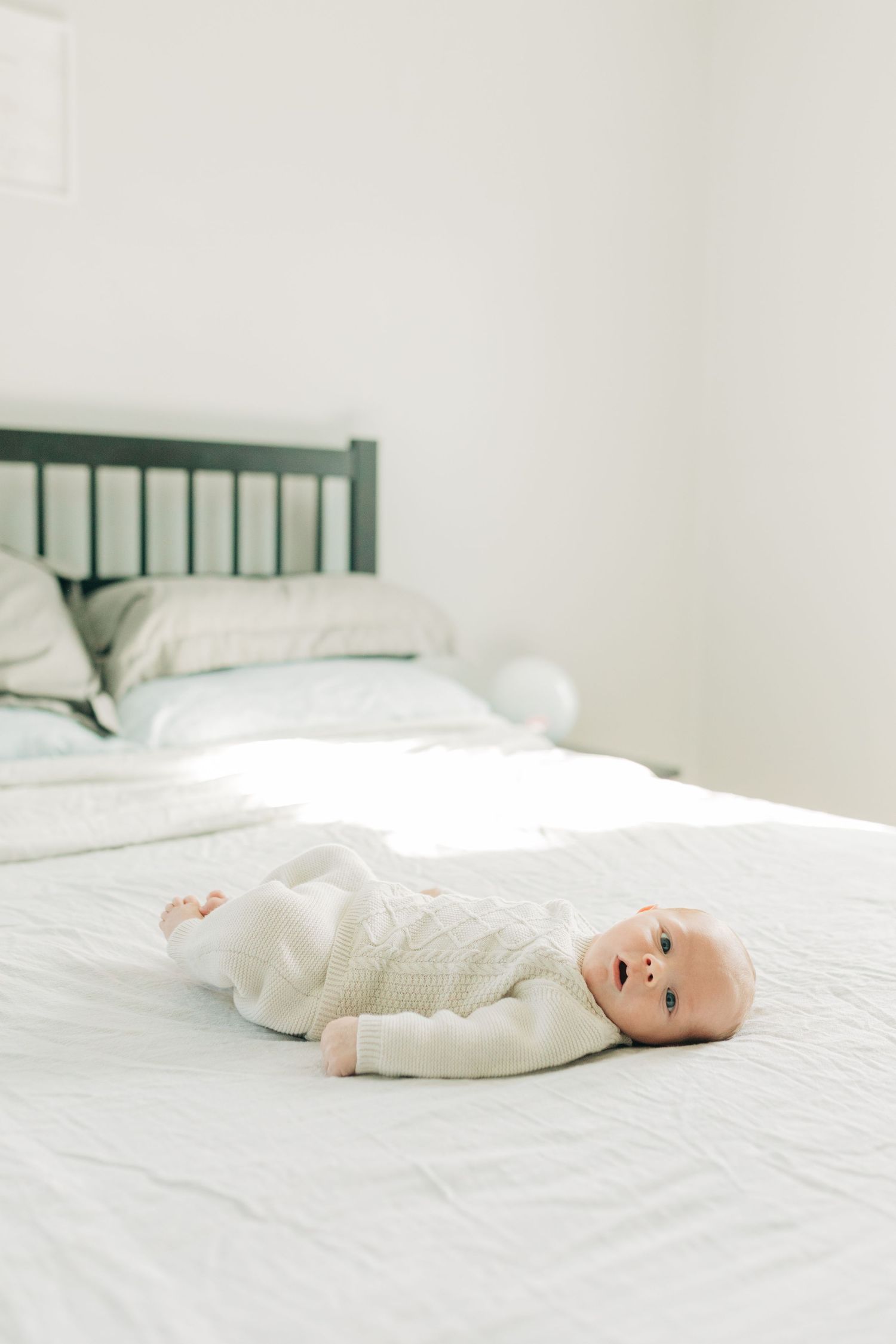 Baby in white knitwear resting peacefully on white bedding.
