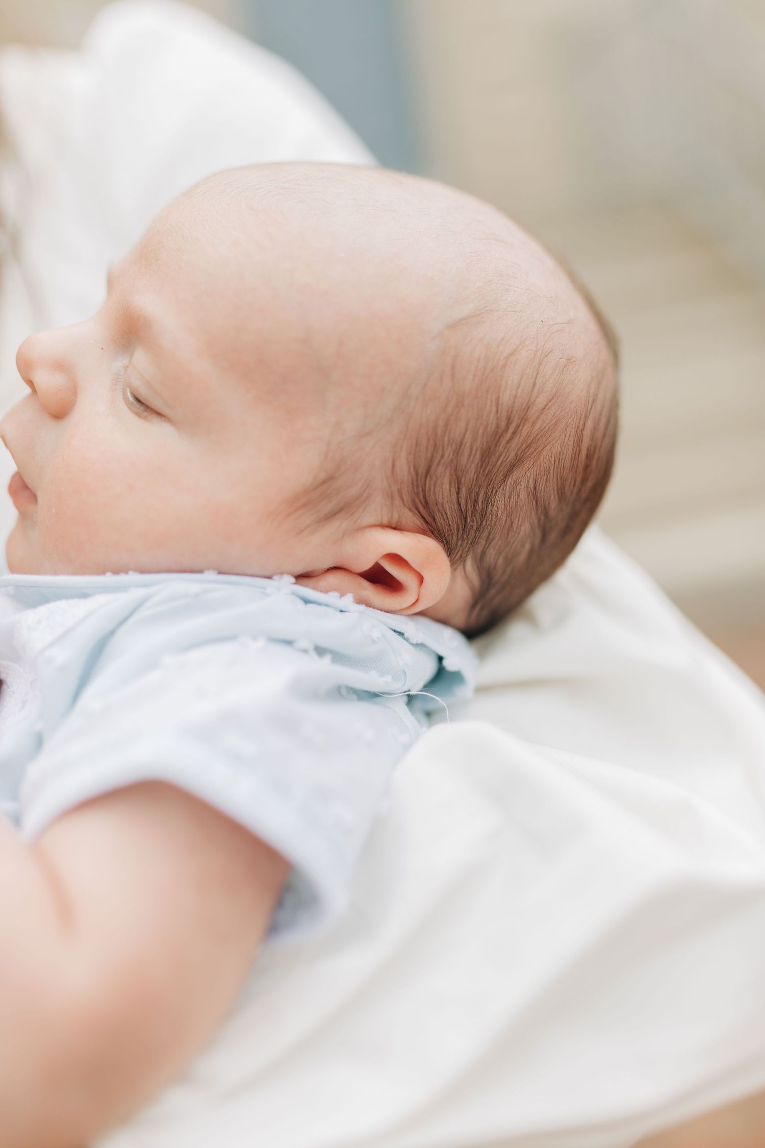 Sleeping newborn baby in soft white clothing against light background.