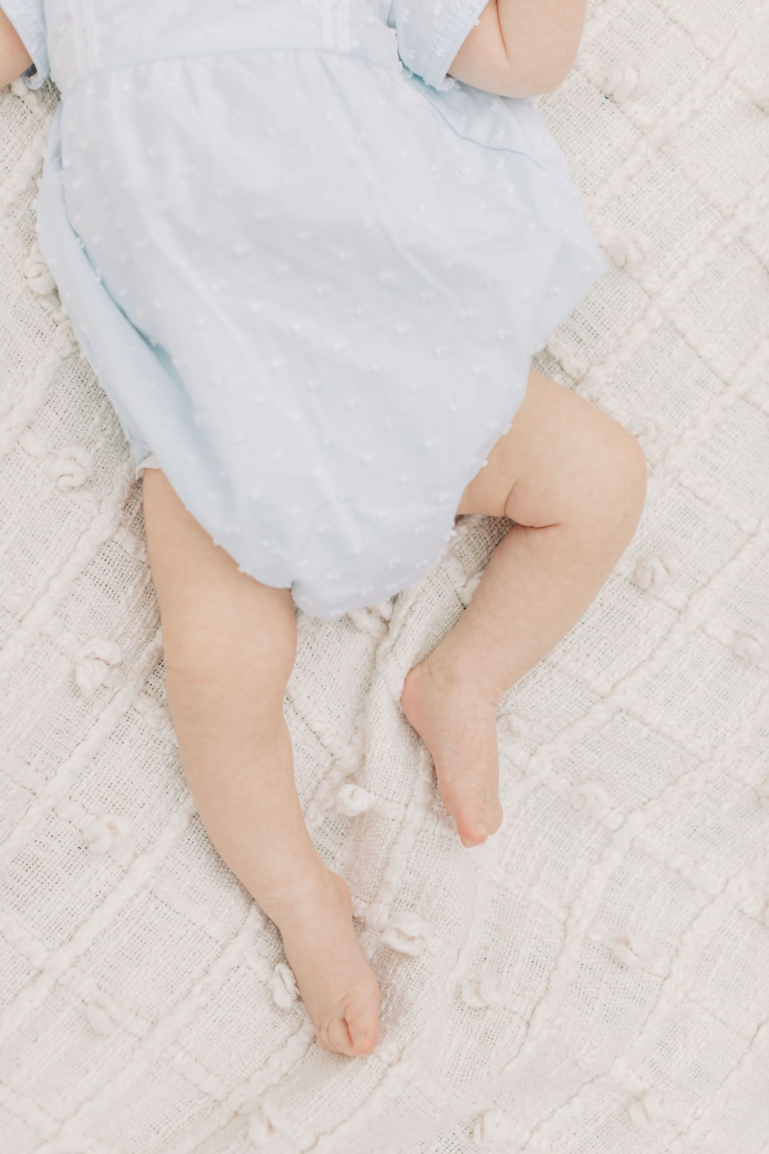 Small bare feet and legs with light blue dress against white fabric.