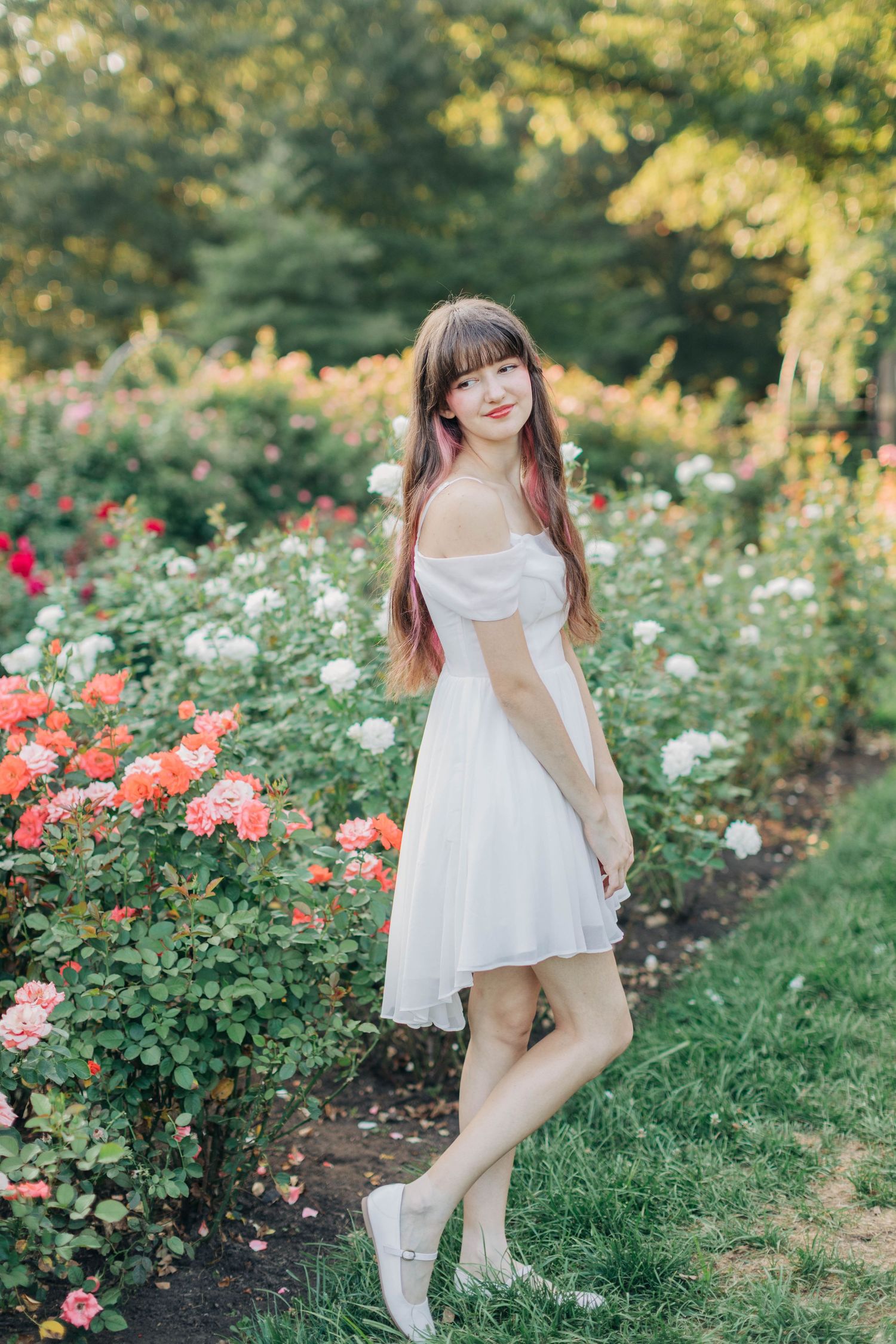 Whimsical garden photoshoot featuring white sneakers and a breezy summer dress among colorful roses.