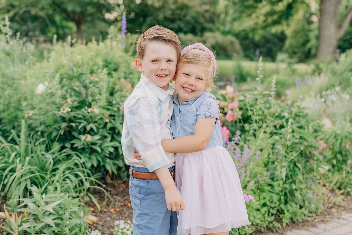 Children laughing and hugging in a lush garden wearing coordinated pastel outfits.