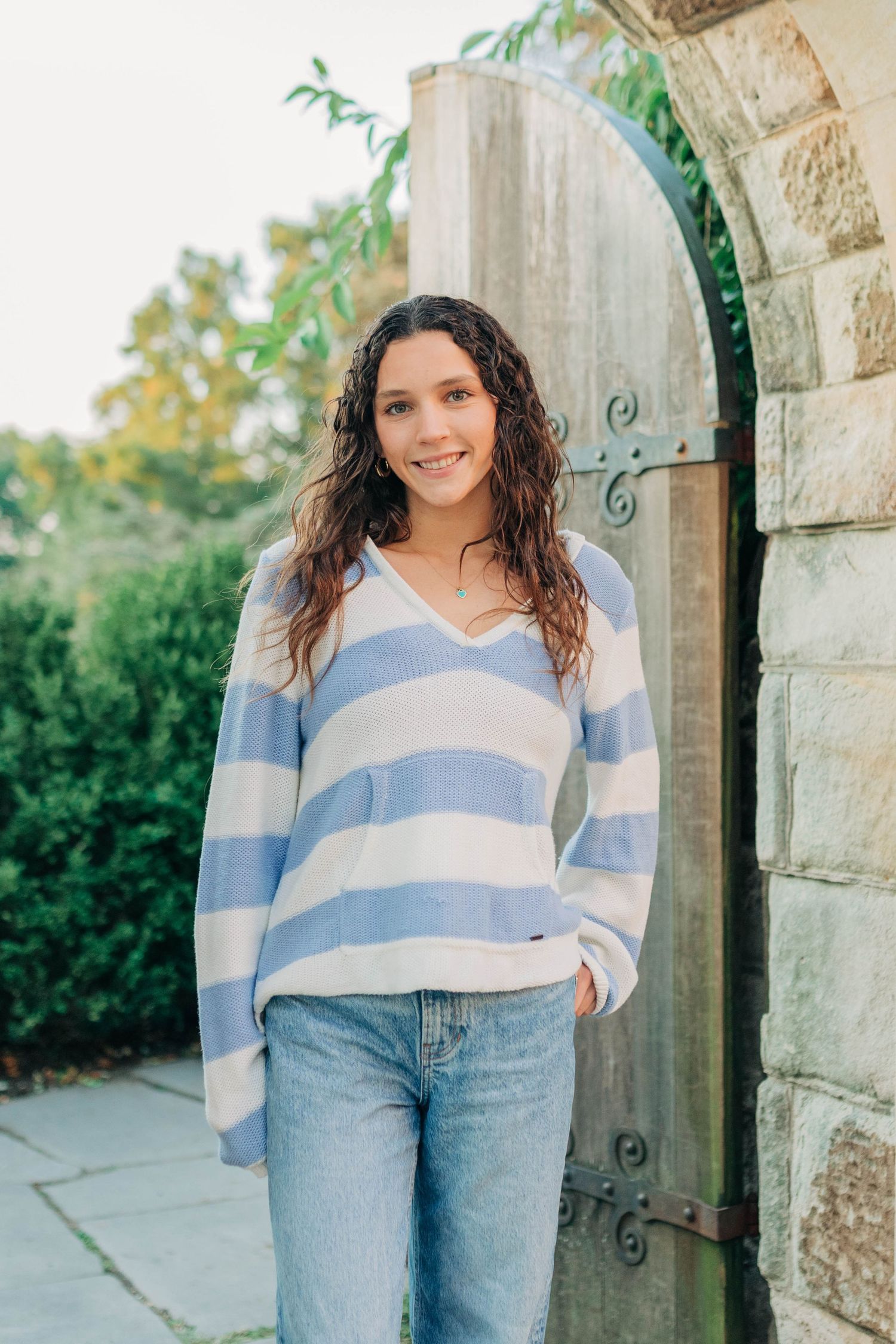 A relaxed pose in a blue striped sweater against stone architectural elements.