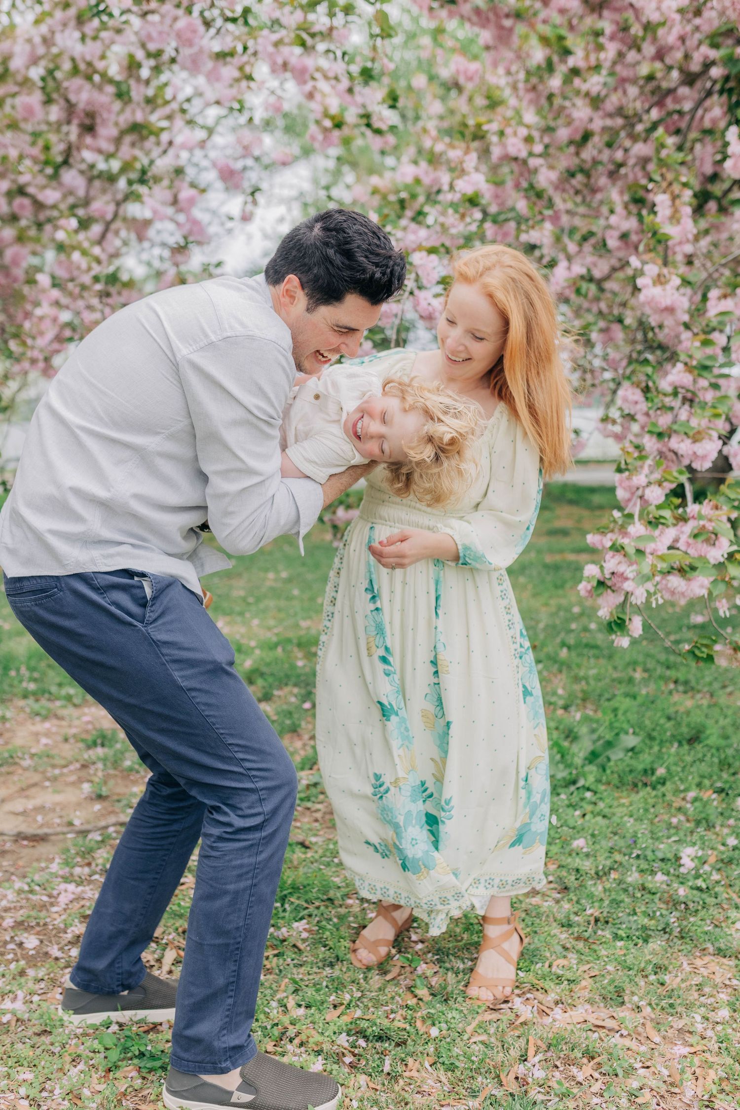 A couple shares a romantic moment under blooming cherry blossom trees in a springtime garden setting.