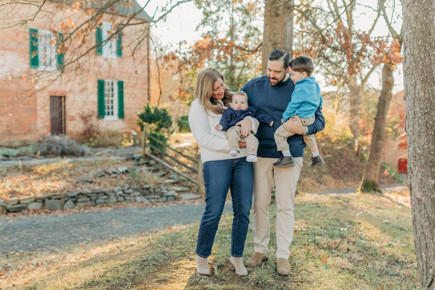 Happy young family with two toddlers posing outdoors near historic brick building in autumn.