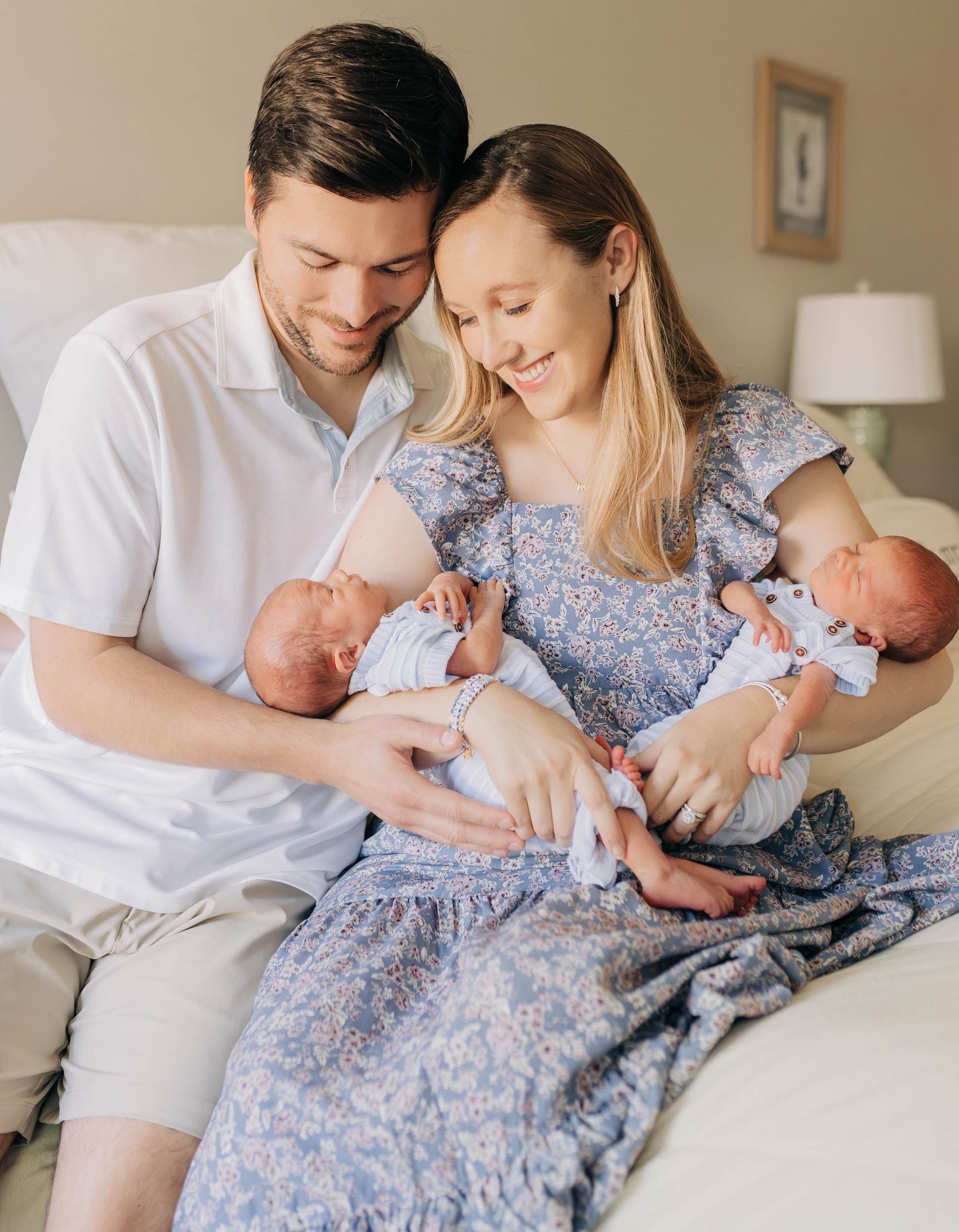 Happy couple sitting on a bed smiling at their newborn twins wrapped in blue blankets.