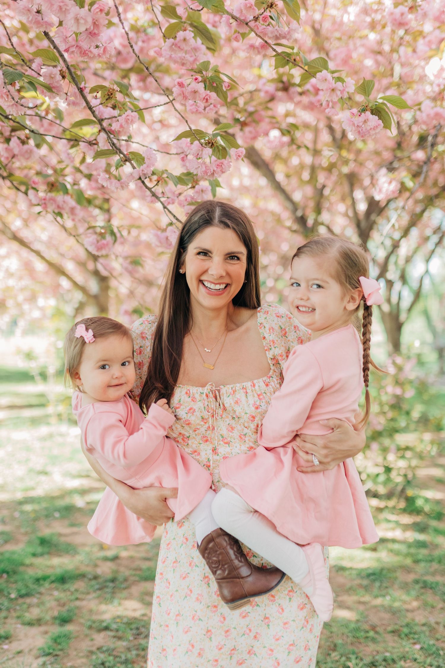 Mother and children in matching pink outfits pose under blooming cherry blossoms.