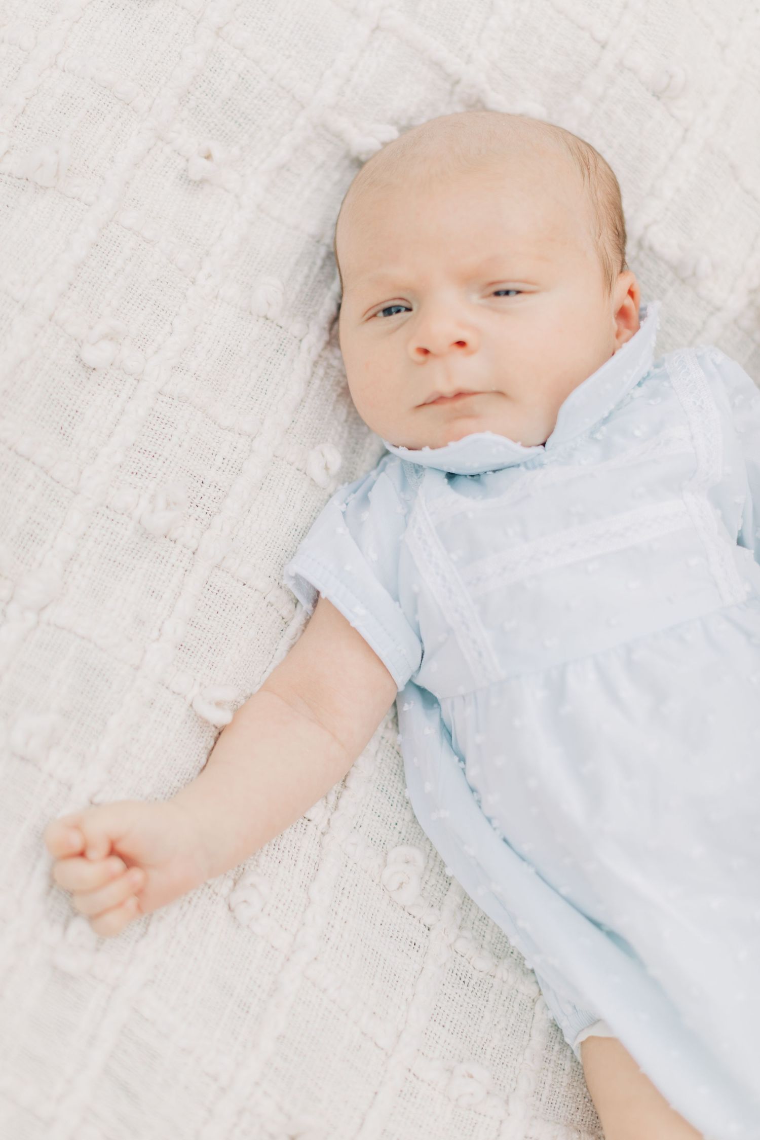 Baby wearing light blue outfit lying on white textured blanket.