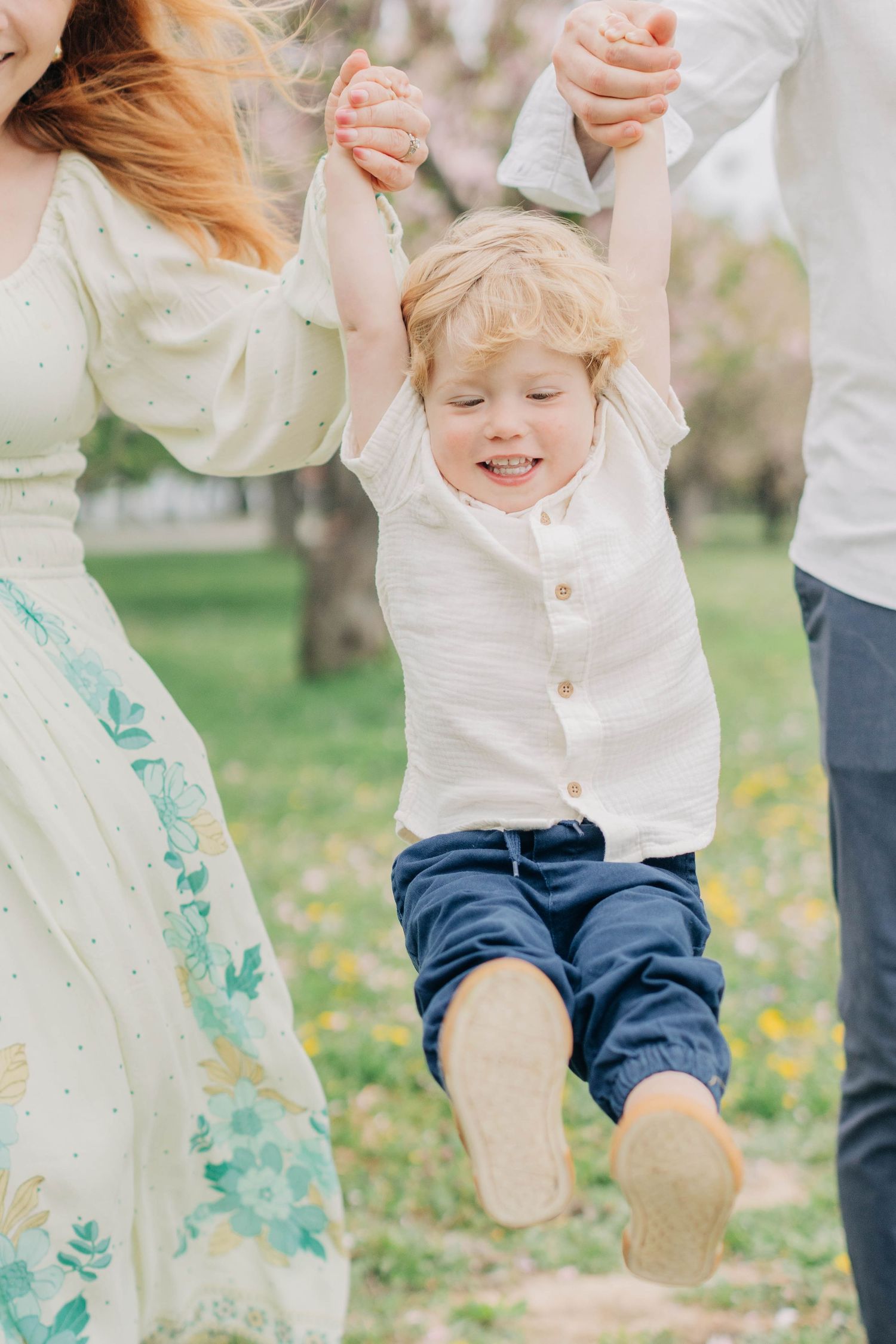 Child wearing white shirt and blue pants jumps playfully in a spring garden with scattered pink petals.
