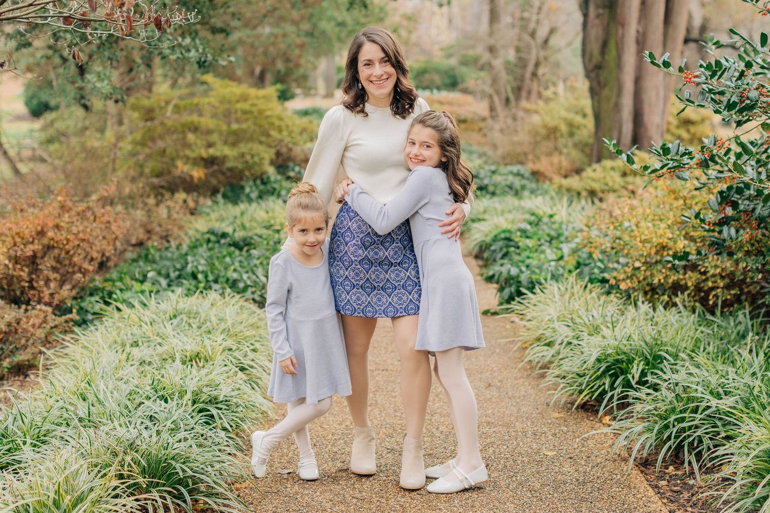 Three people in coordinating outfits pose together on a garden pathway.