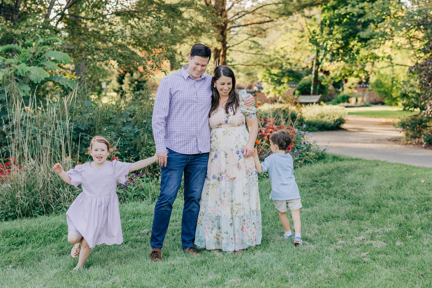 Happy family of four holding hands and smiling together in a lush garden park setting.