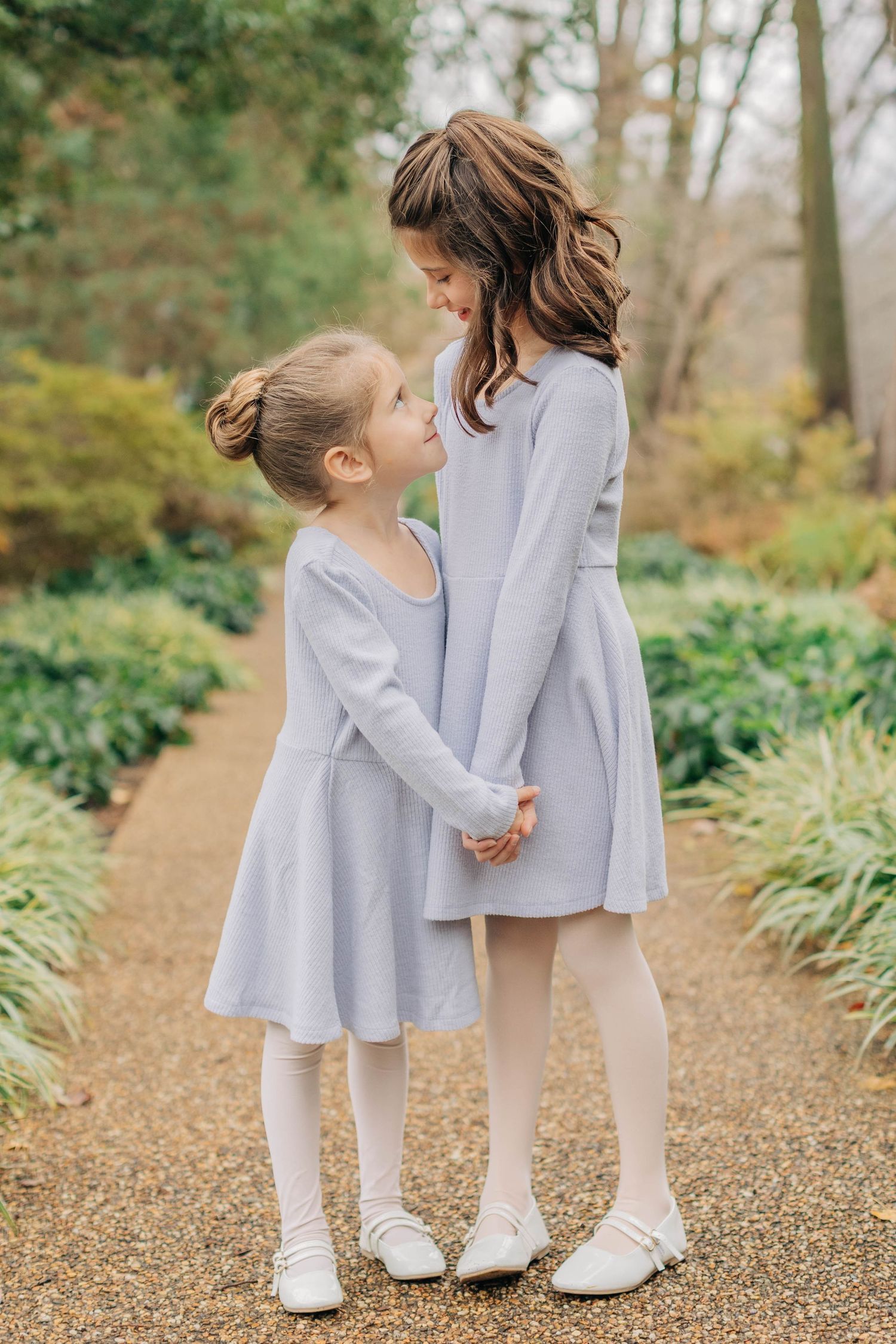 Two people in matching grey dresses share an intimate moment on a garden path.