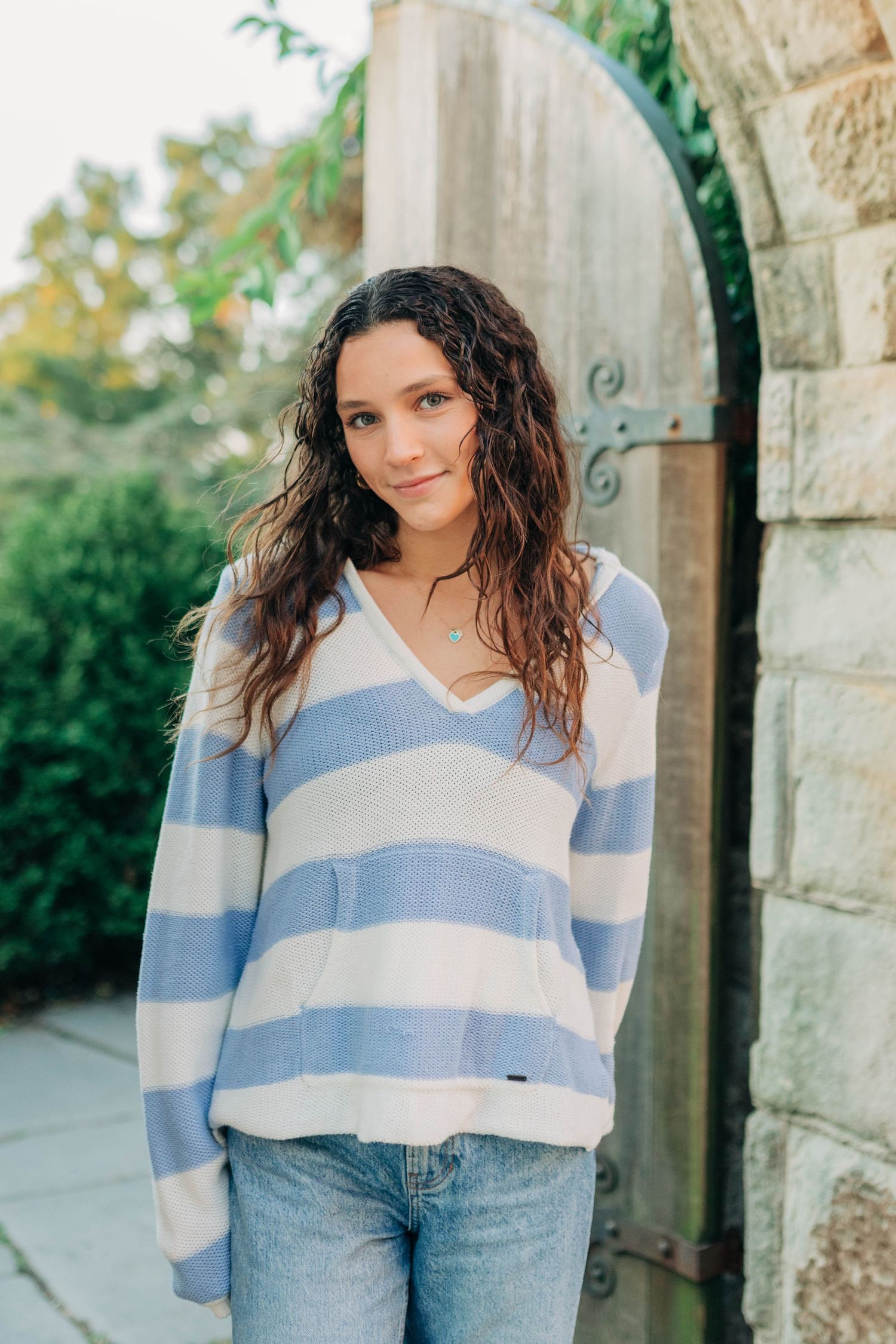 A person in a striped blue and white sweater and jeans poses against stone architecture.