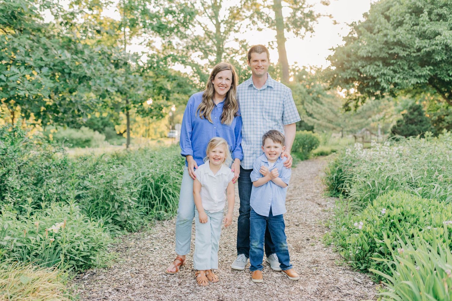 Natural outdoor family portrait session on a wooded path during sunset.