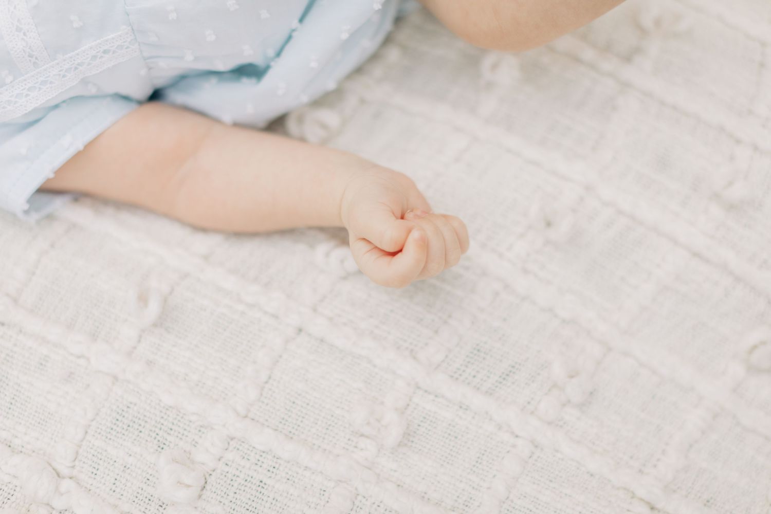 Baby's small fist and arm against a white blanket background.