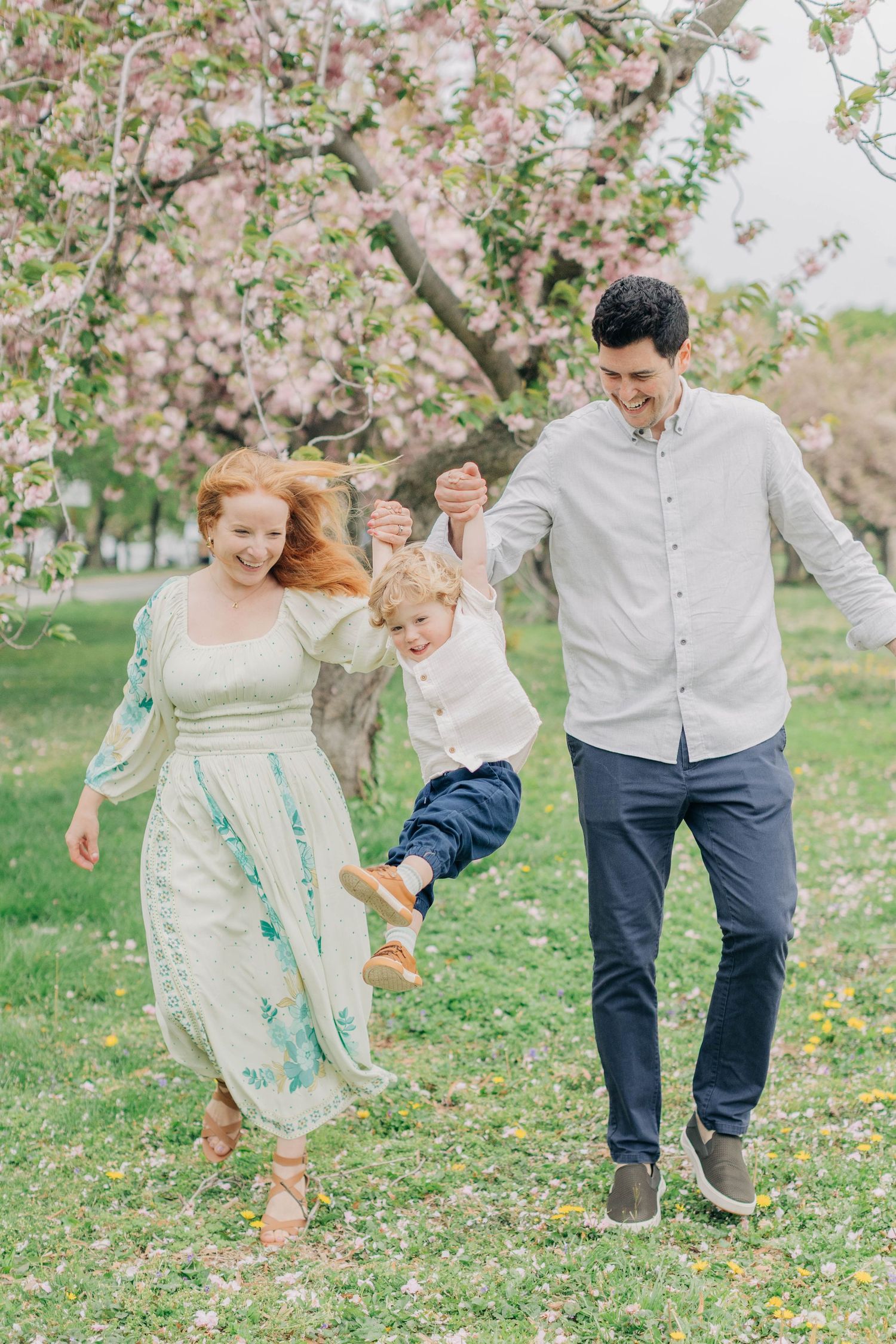 A family plays together under blooming cherry trees in a spring garden setting.