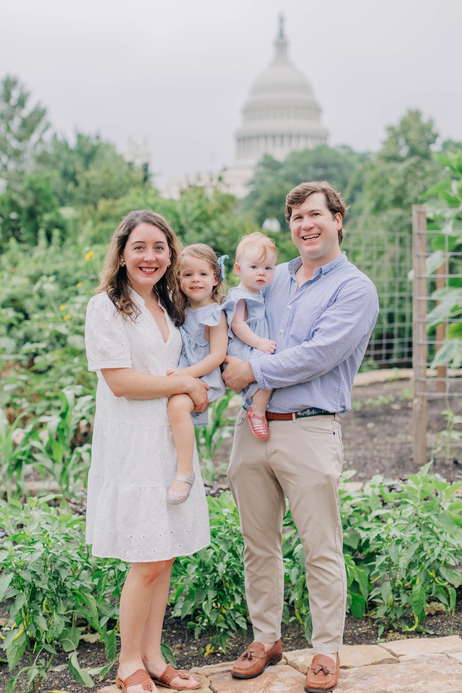 Family of four posing in a garden with the U.S. Capitol building in the background on a cloudy day.