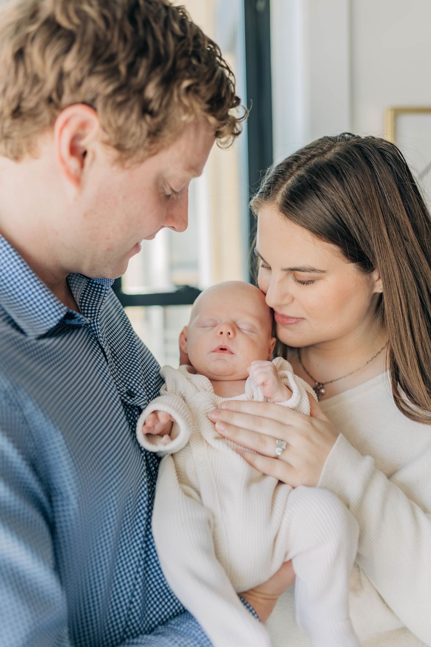 A couple tenderly gazes at their sleeping newborn baby dressed in white.