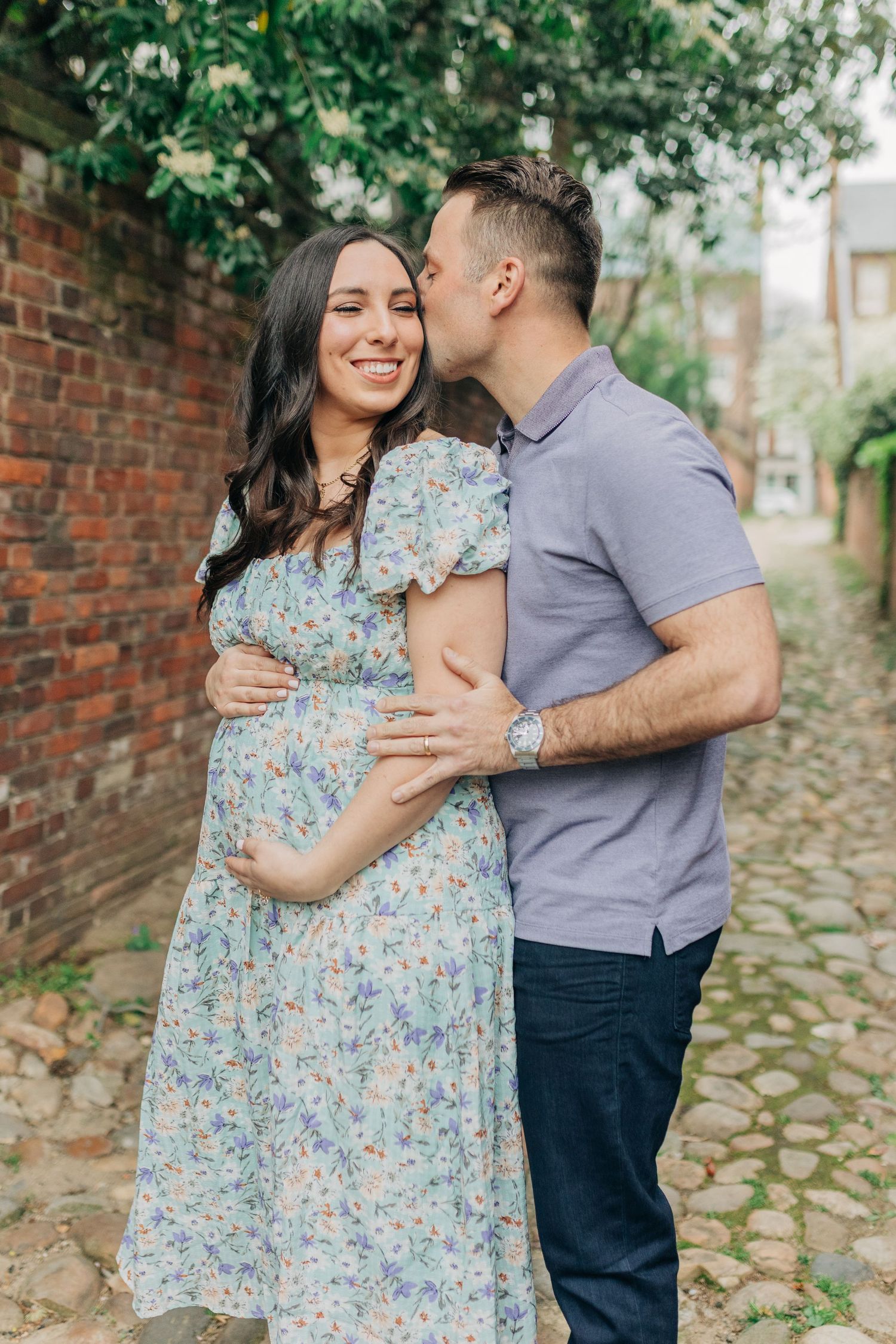A couple embraces on a historic cobblestone path while wearing casual spring attire.