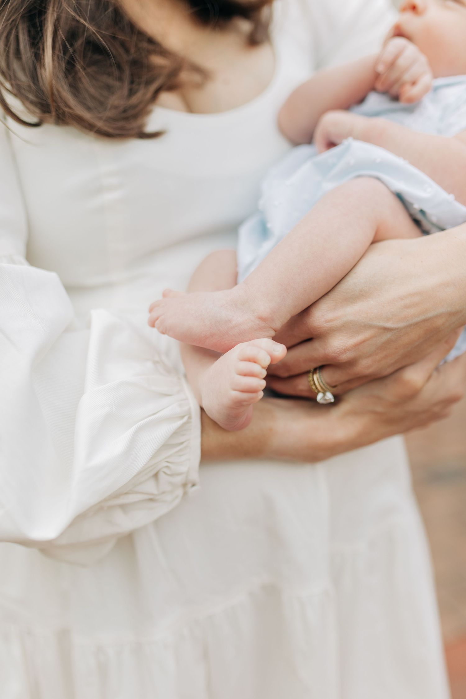 Close-up of hands holding and comforting a newborn baby in white clothing.
