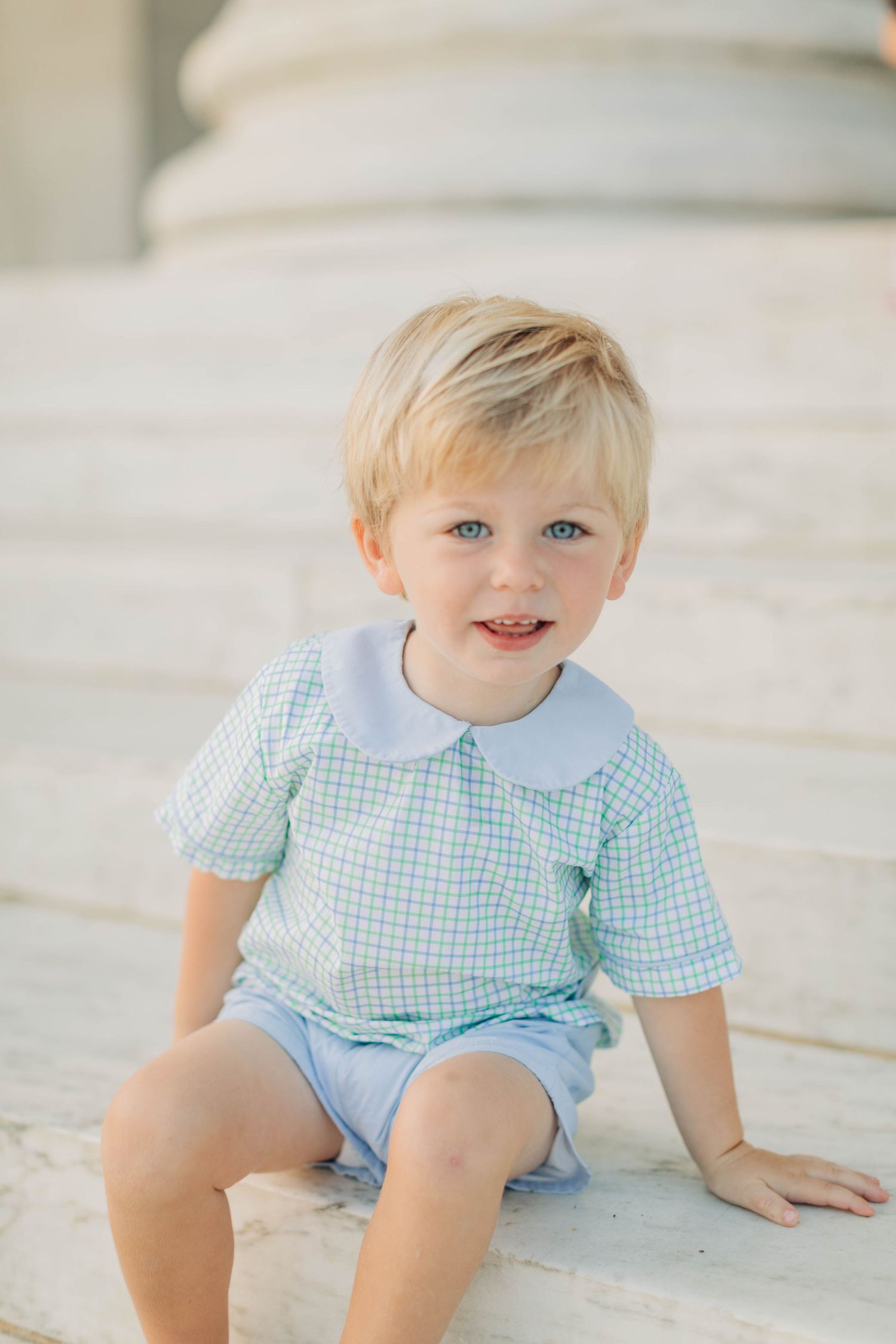 Child in blue gingham outfit sitting on marble steps during a portrait session.