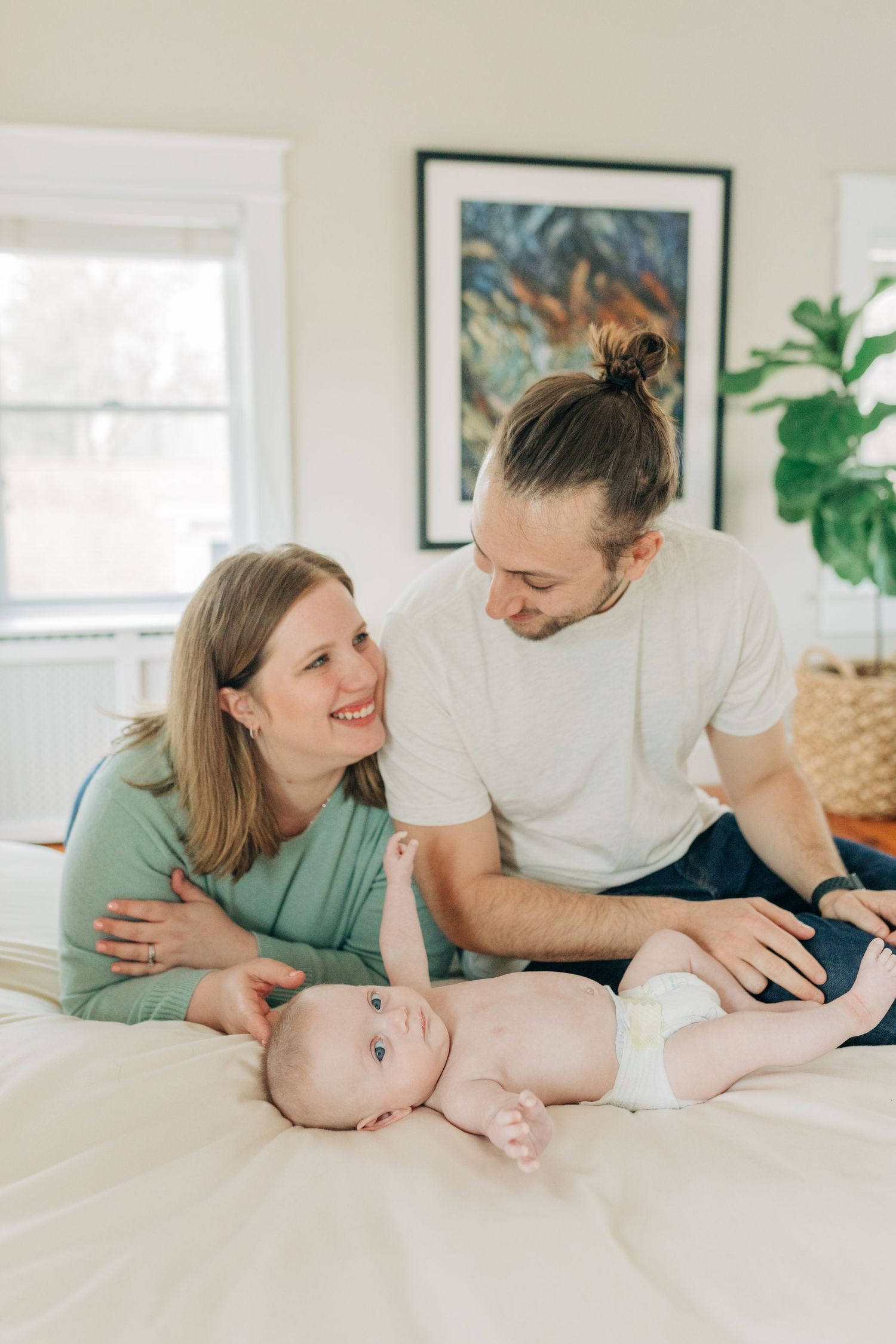 Parents sharing joyful moments with baby on white bedding in bright room.