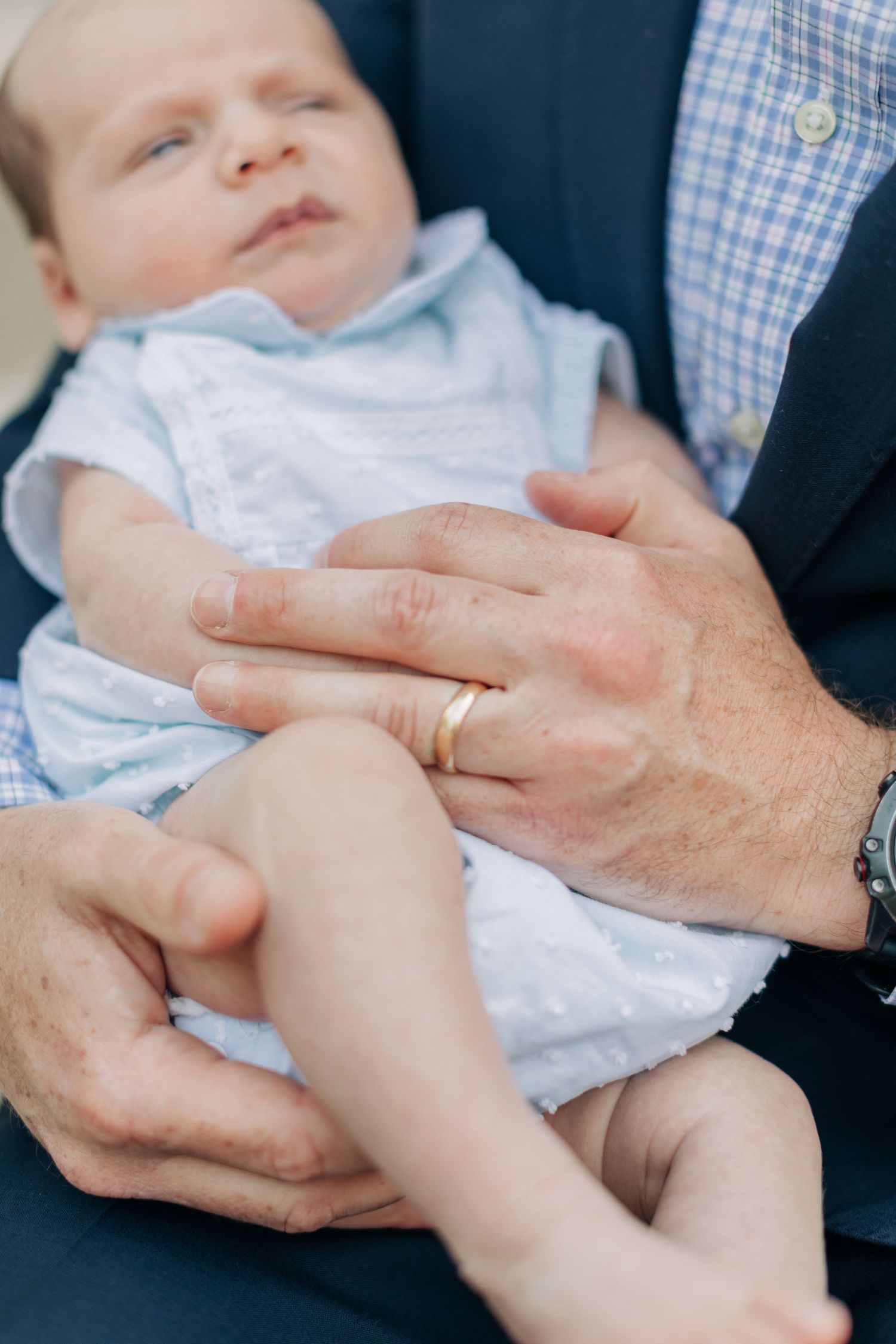 Close-up detail of hands holding a baby wearing a light blue outfit.