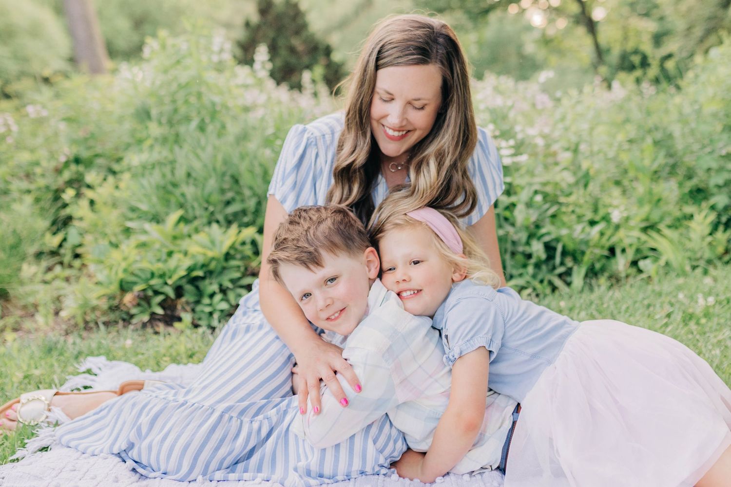 A sweet outdoor family photoshoot on a blanket in a grassy field on a sunny day.