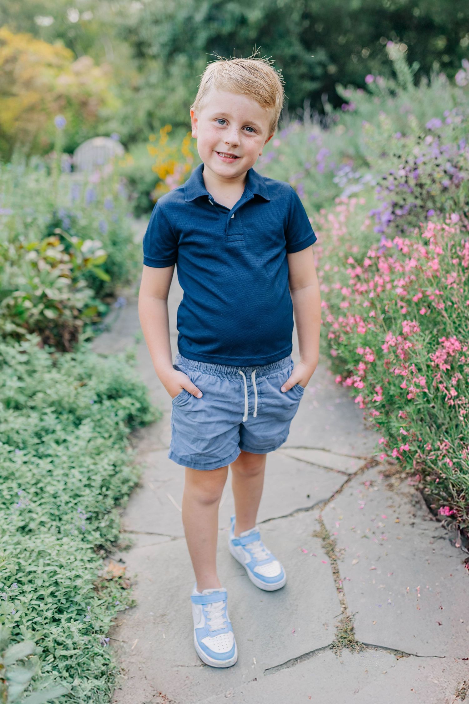 Child in navy blue outfit walking along a garden path with pink flowers.