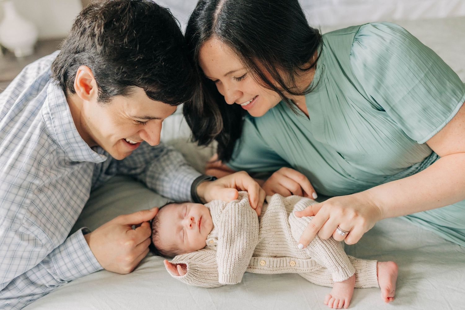 Parents sharing an intimate moment with their newborn baby on white bedding.