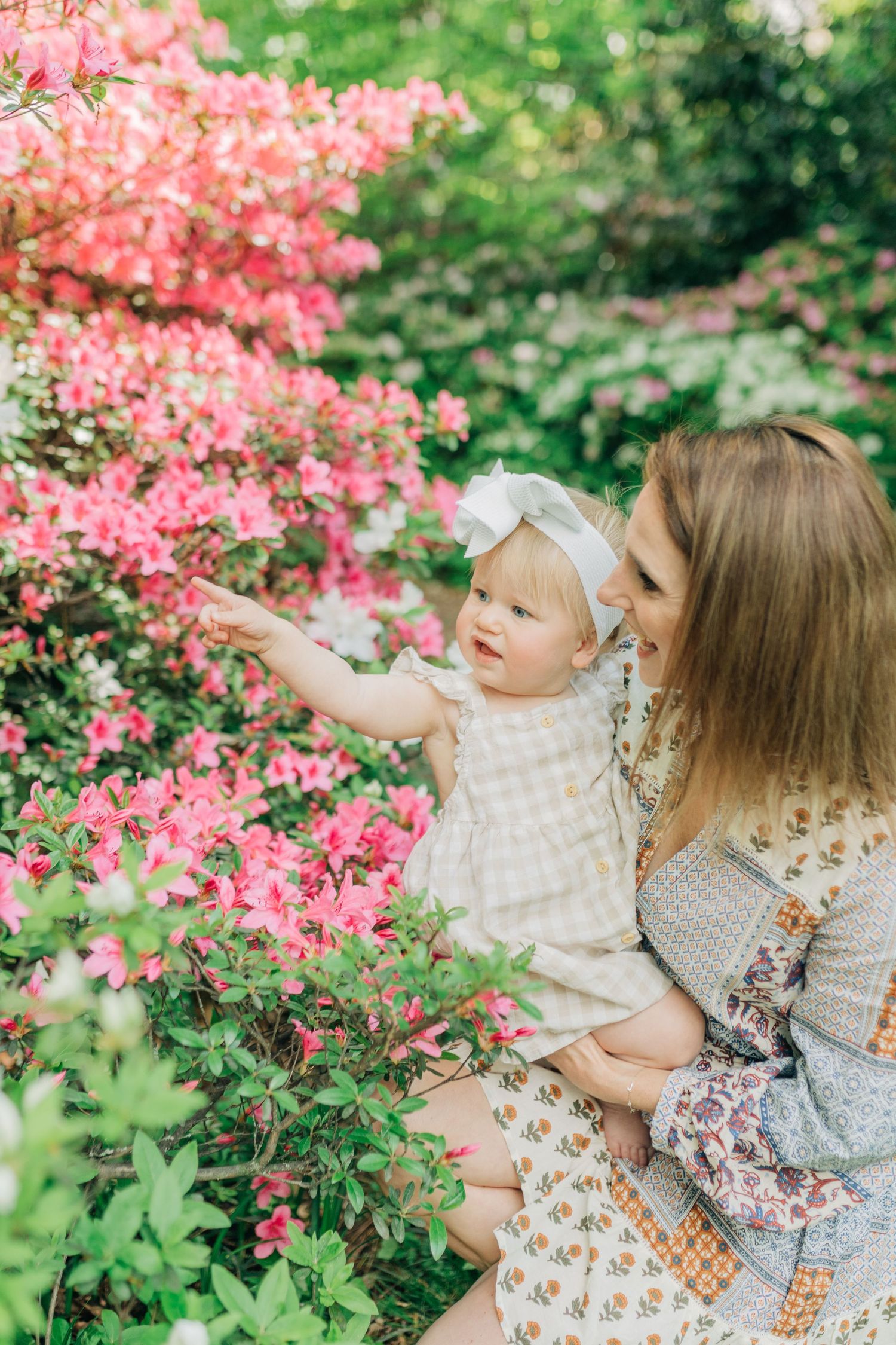 Mother and child sitting among pink azalea bushes in spring garden setting.