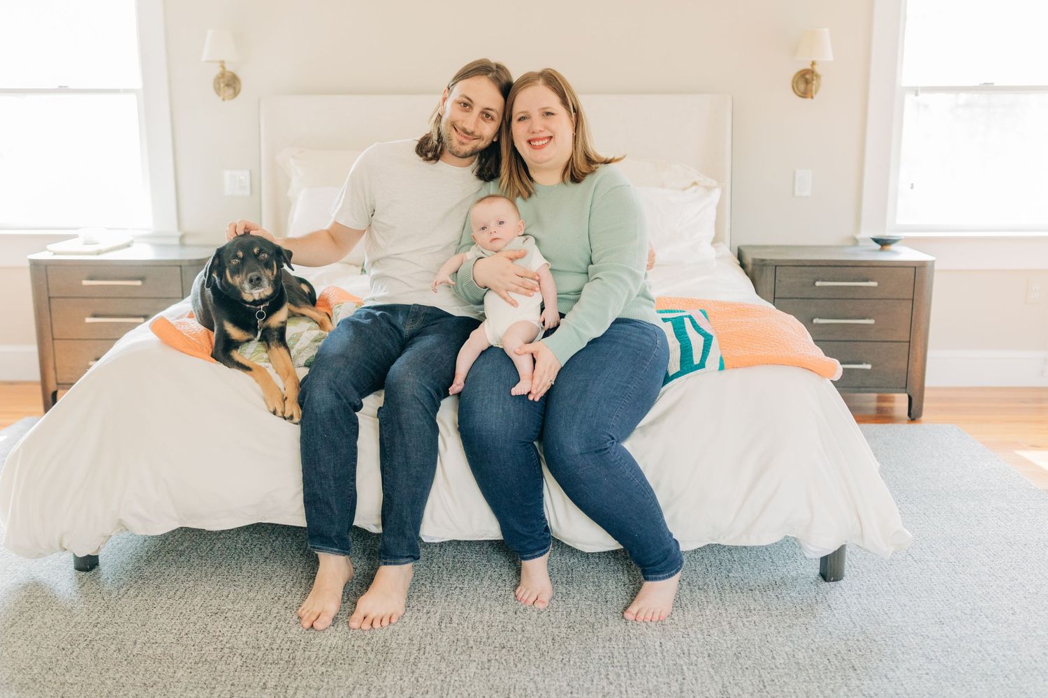Casual family moment captured on white bed with orange accent pillow.