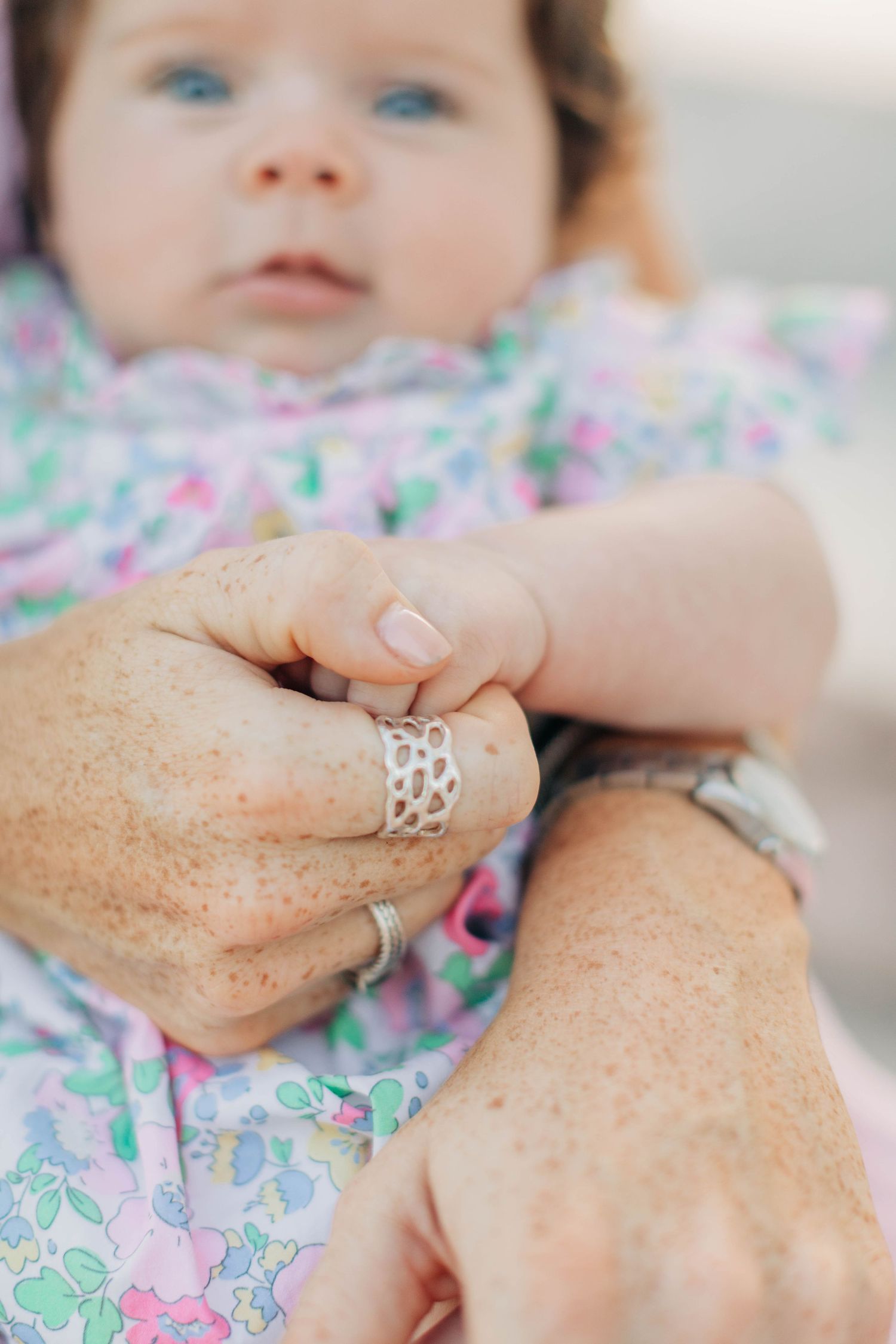 Close-up of hands holding baby wearing floral print outfit.