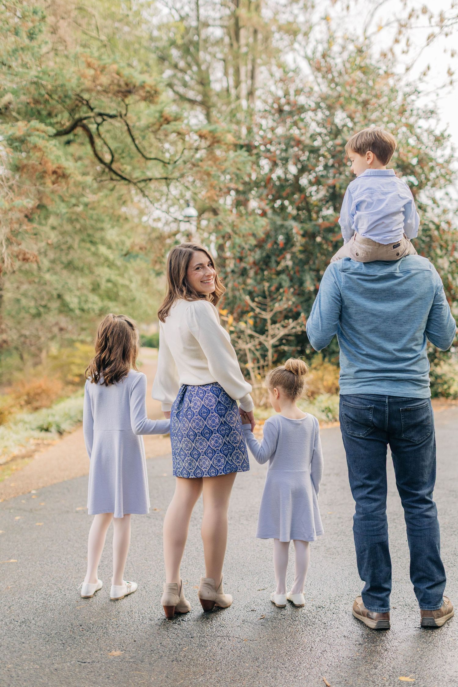 A family of four walks together on a tree-lined path during autumn.
