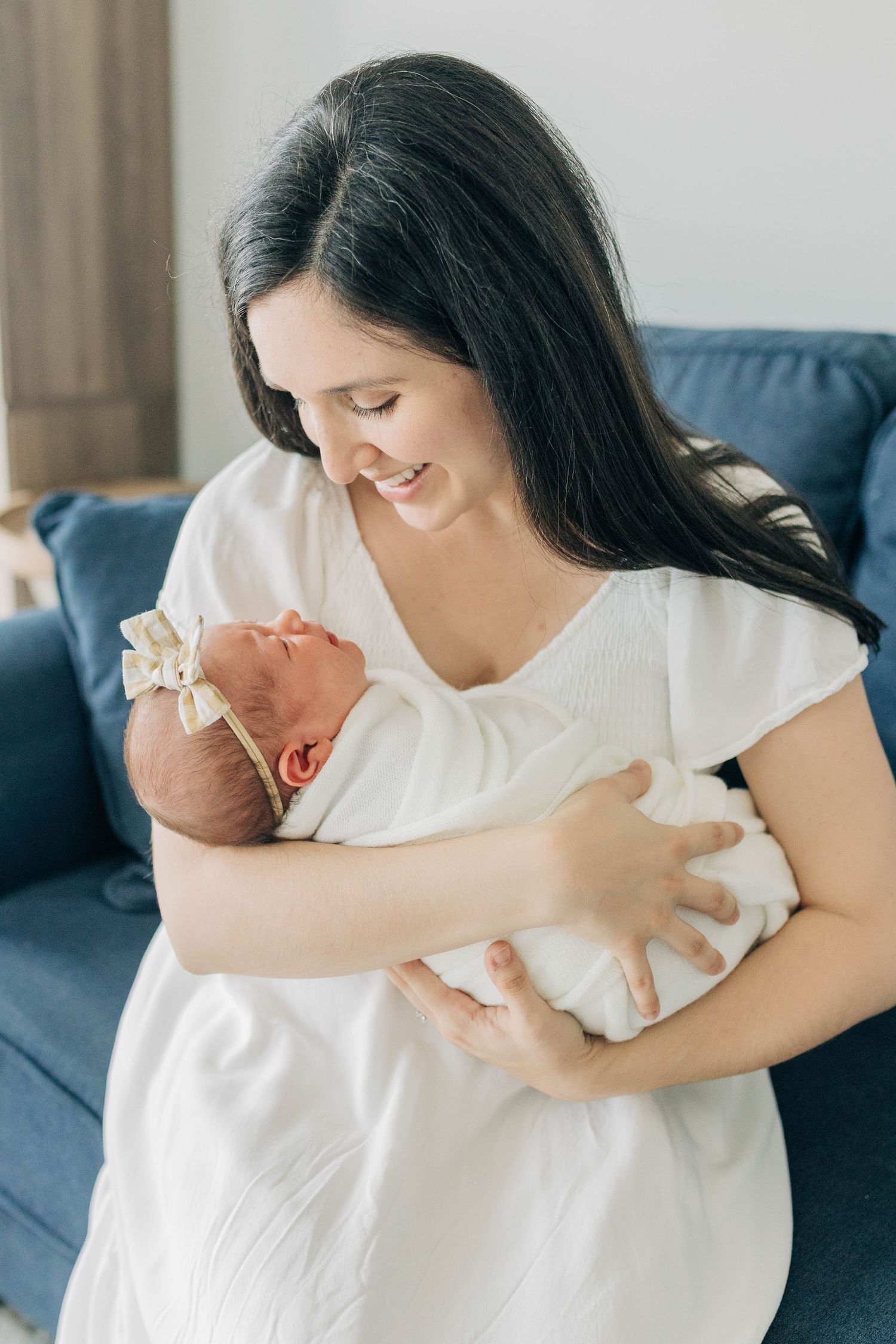 Tender moments between parent and baby on a blue couch in natural light.