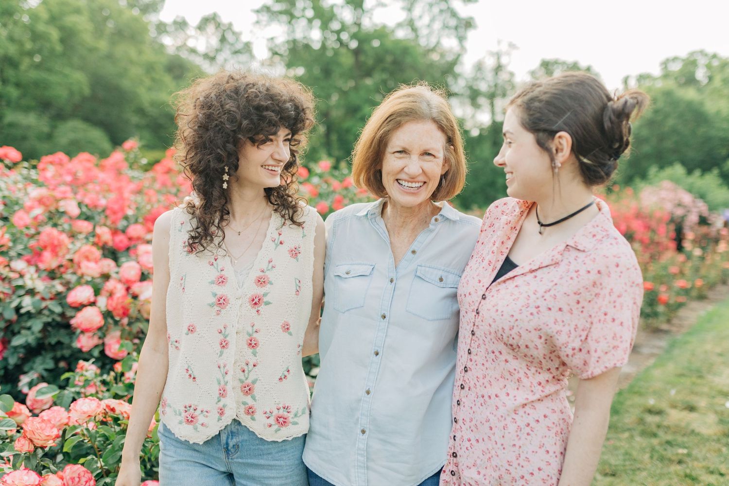 Three people pose casually together in a garden path surrounded by blooming roses.