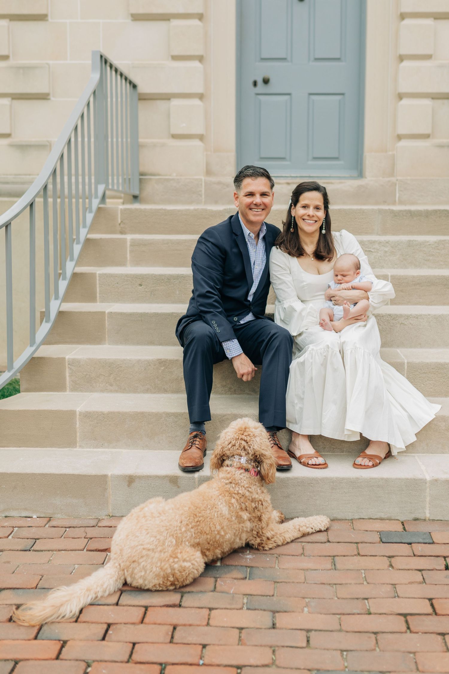 Family sitting on brick steps with their goldendoodle dog lying at their feet.