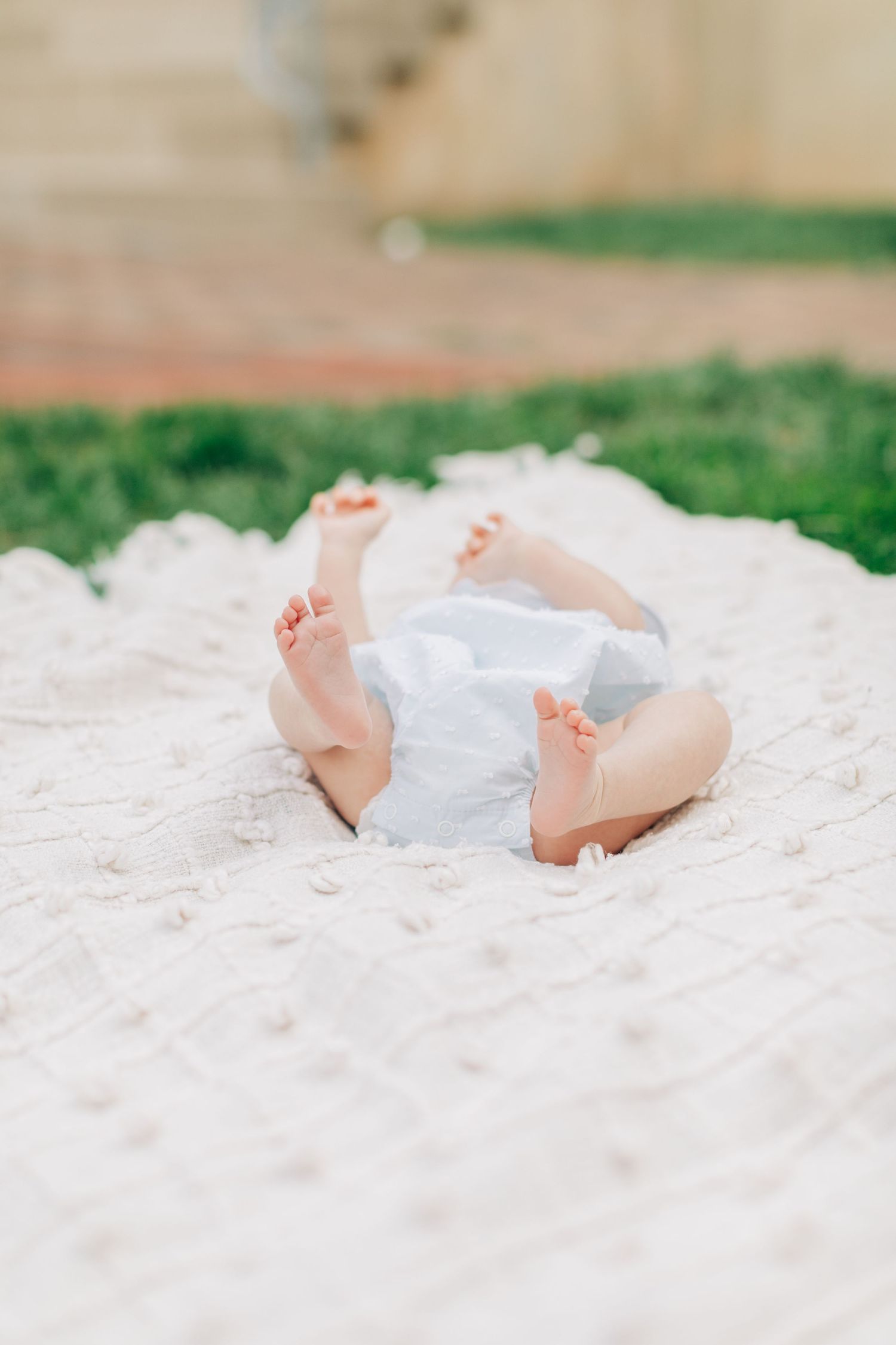 Small baby feet peeking out against white blanket with grass in background.