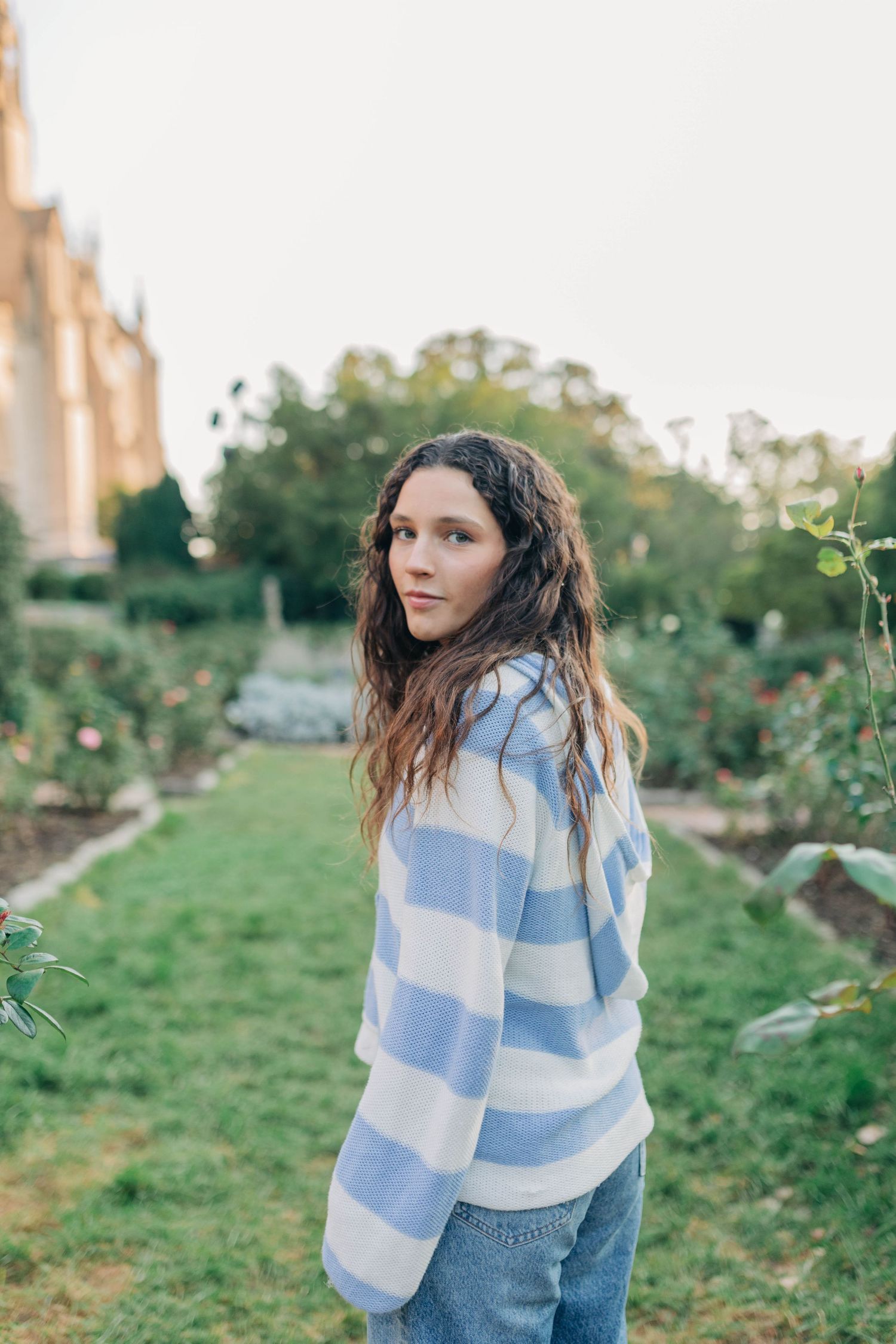 A person wearing a blue and white striped sweater poses outdoors against a green garden background.