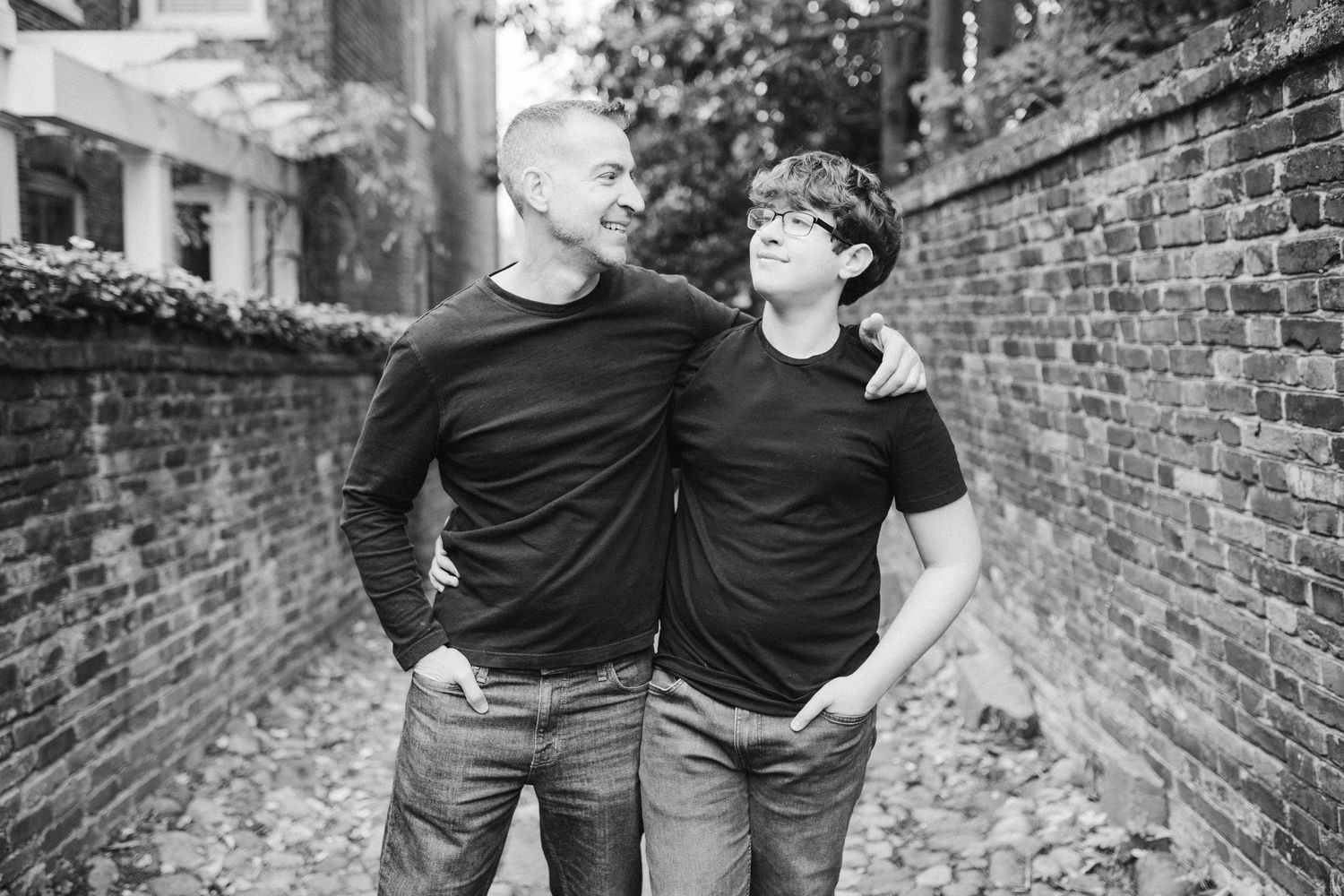 Black and white portrait of two people in dark shirts standing by a brick wall.