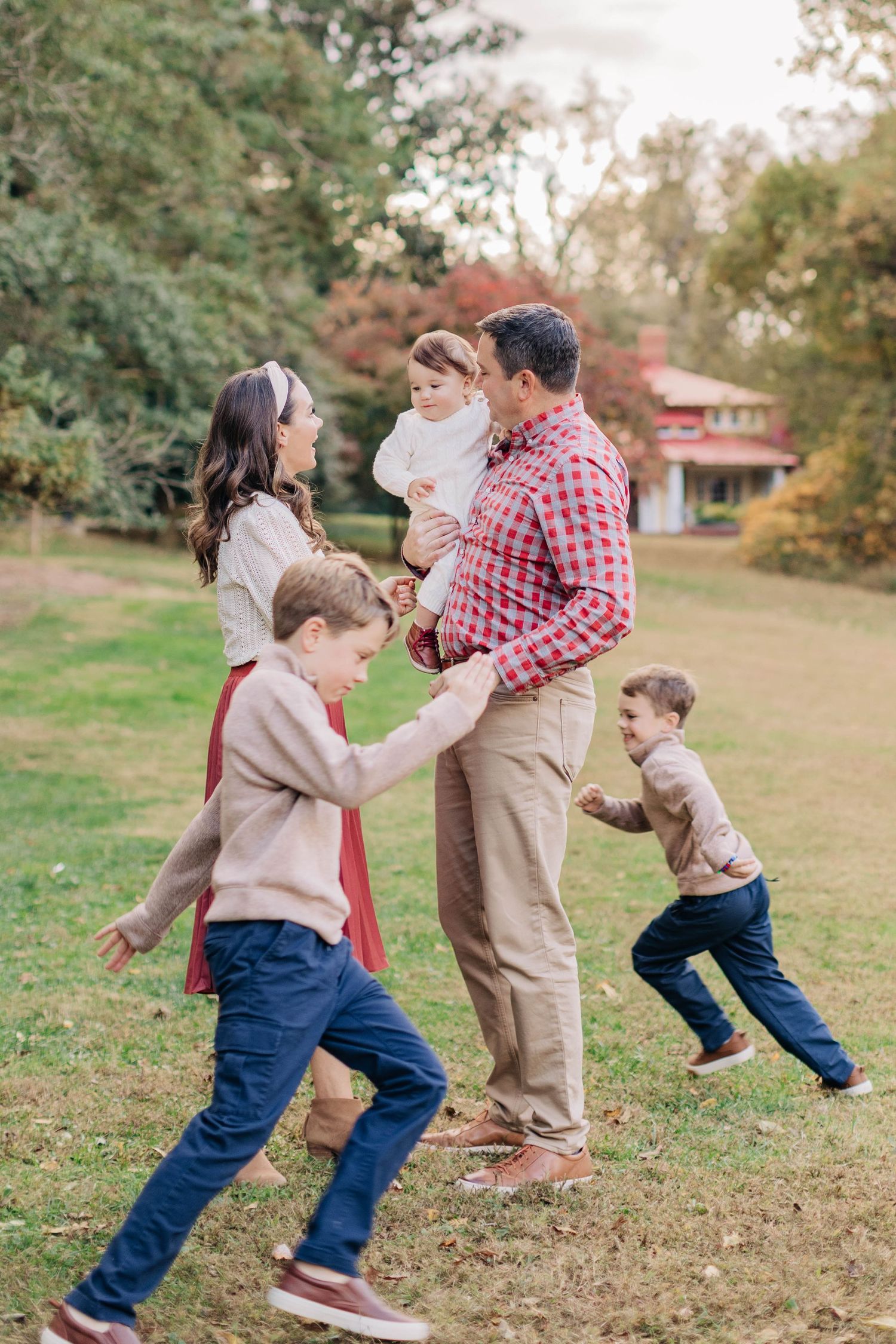 A family plays and runs together in a grassy park during autumn.