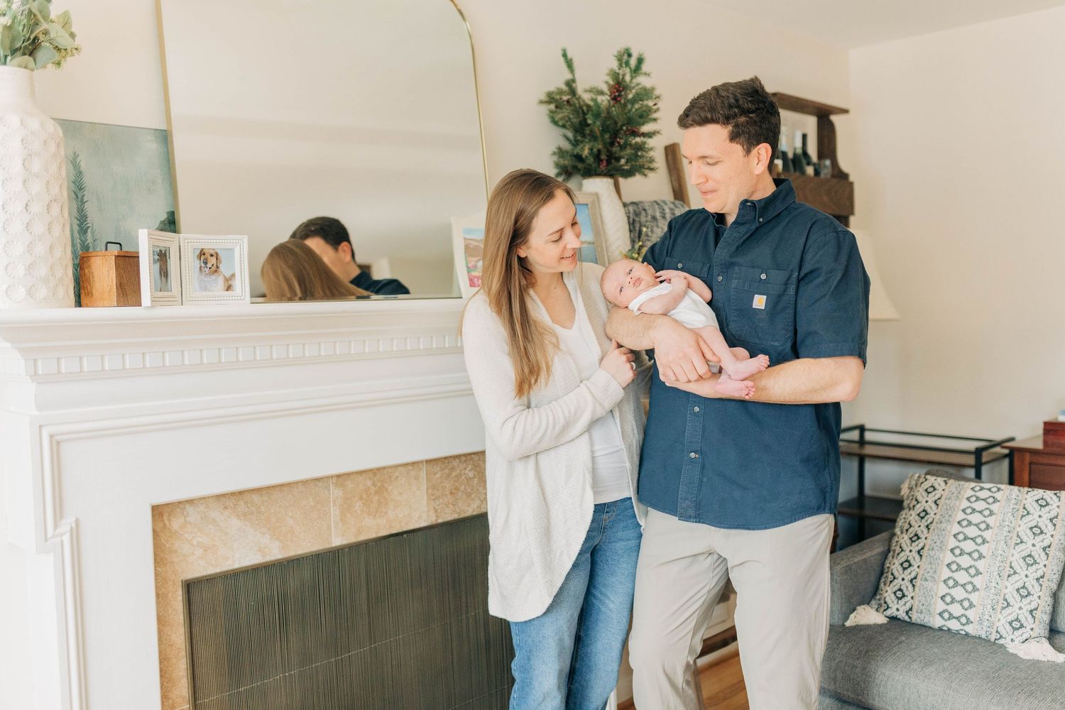 Parents sharing joyful moment with baby by fireplace in living room.