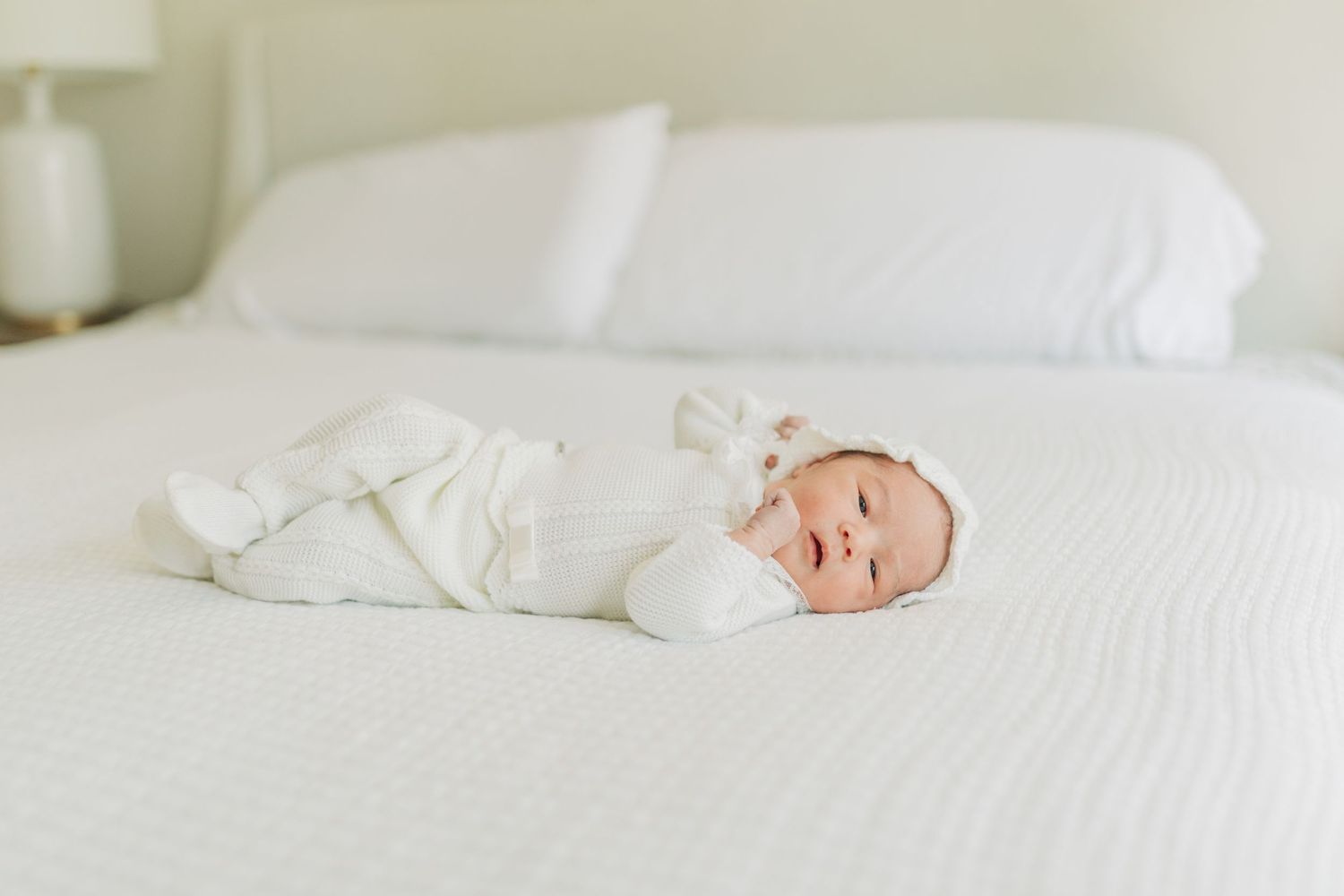 Baby in white outfit resting peacefully on crisp white bedding.