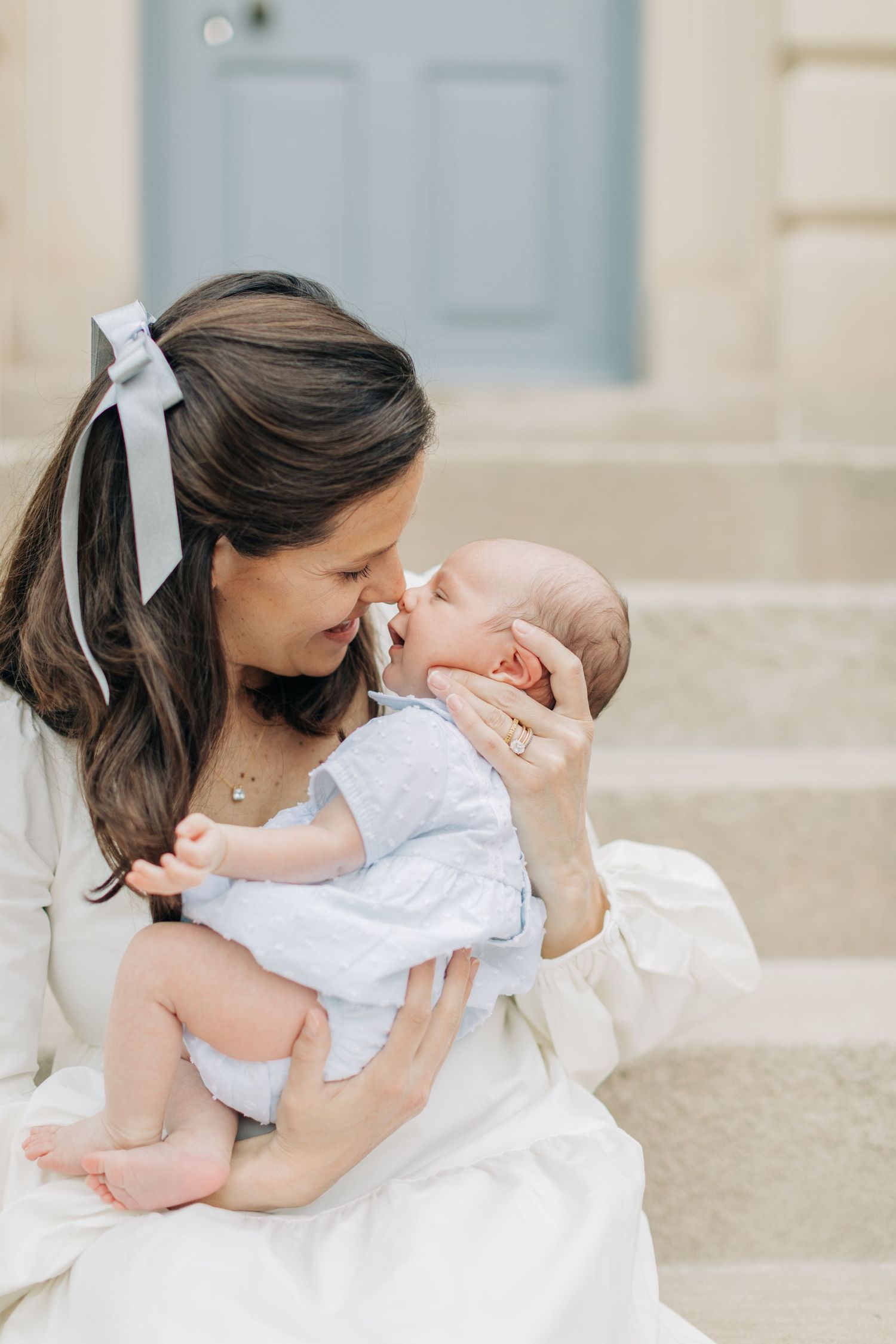 Mother in white dress embraces baby while sitting on stone steps.