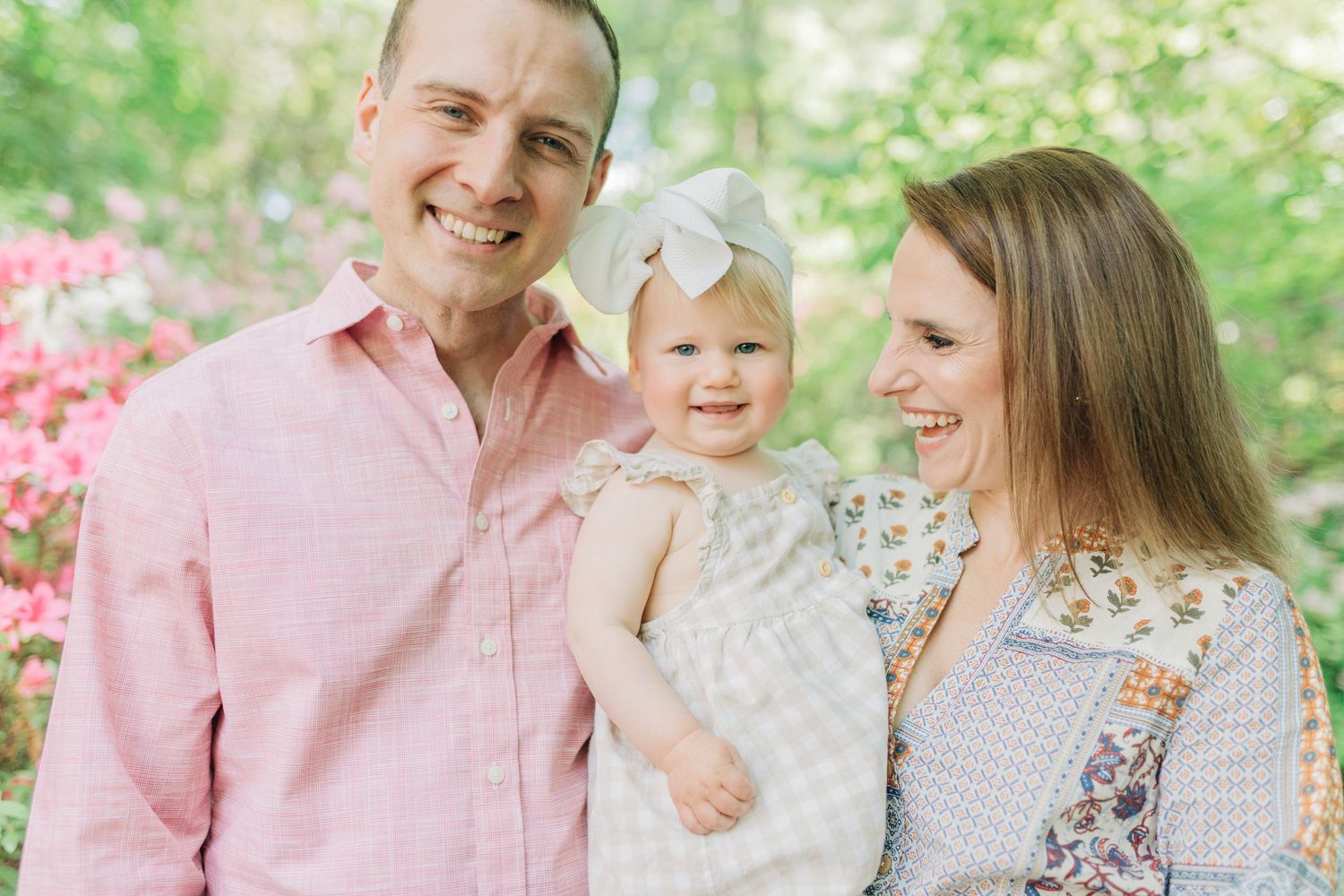 Candid family moment captured in garden setting with pink flowering bushes.