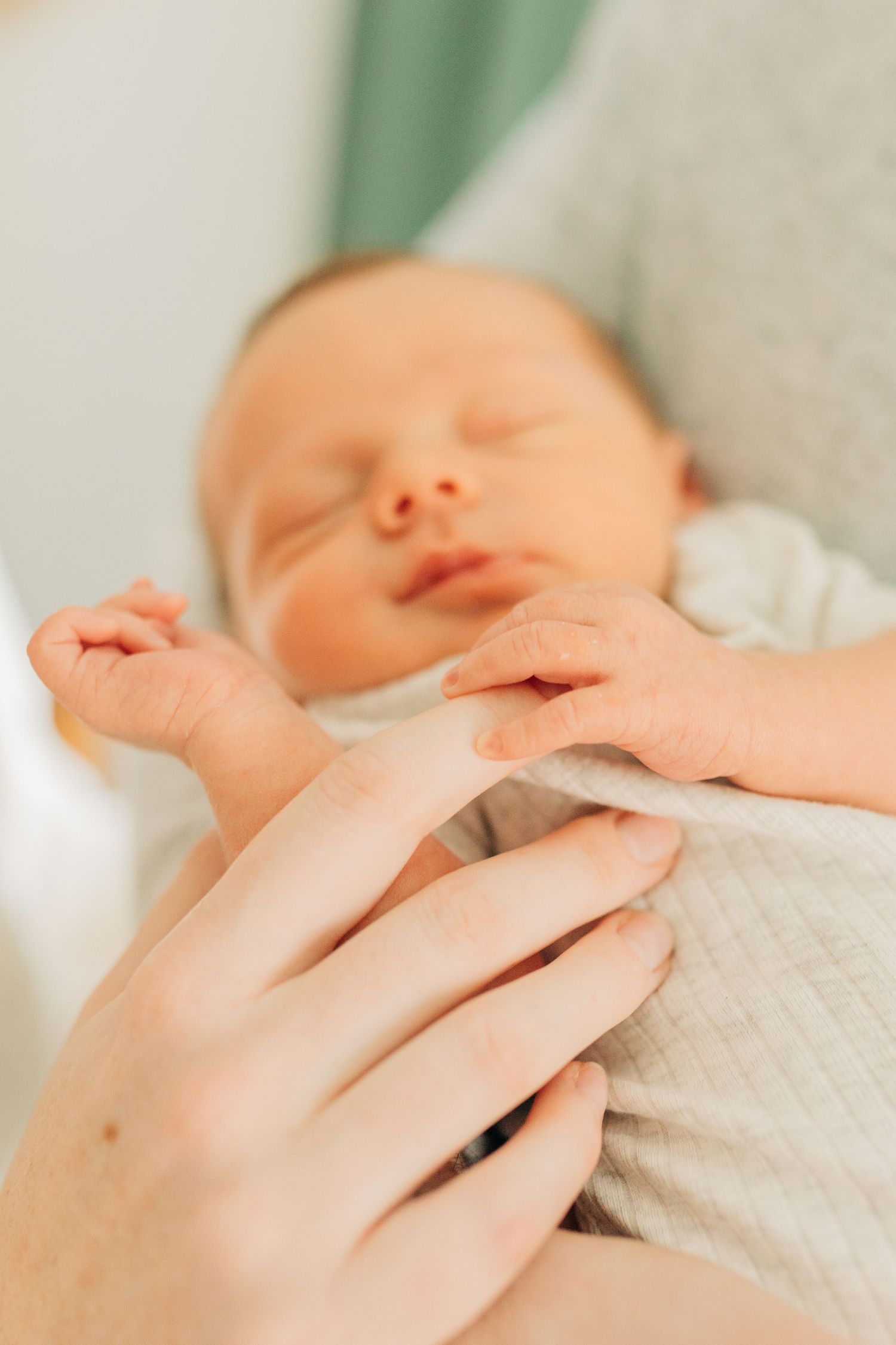 Close up of sleeping newborn baby's face with parent's hands gently touching.
