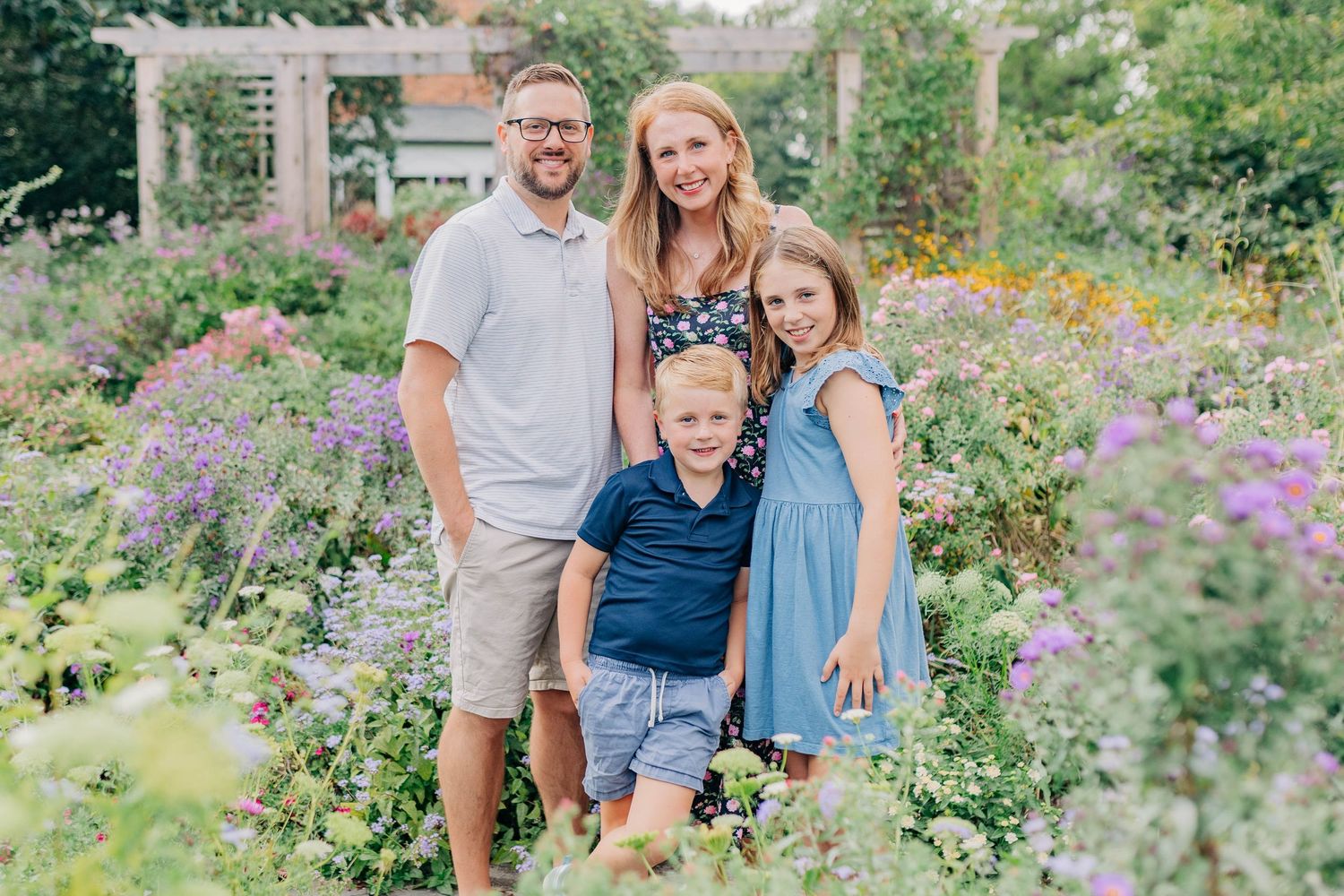 A family of four poses for a portrait in a colorful summer garden with purple flowers.
