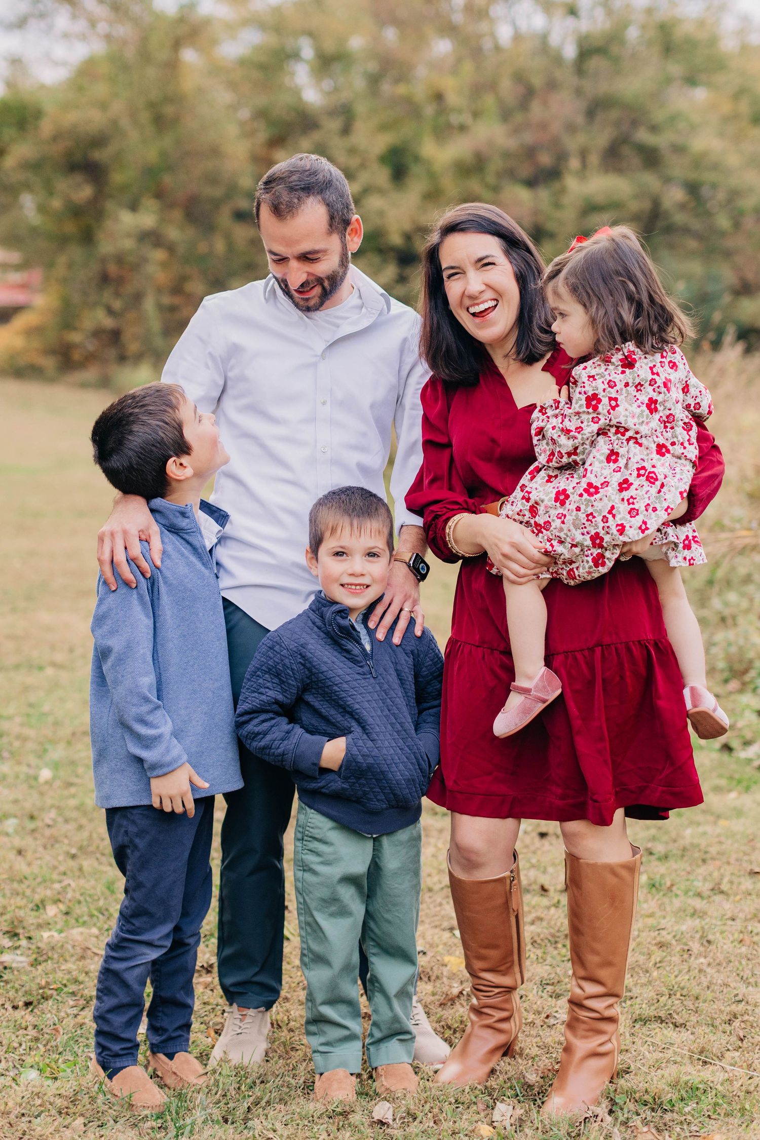 Happy family of five posing outdoors in fall, parents with three young children dressed in coordinated red and blue outfits.