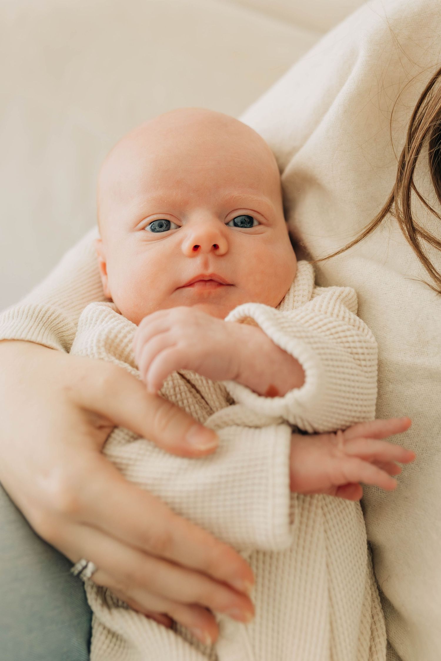 Newborn baby with blue eyes wrapped in a cream waffle blanket, cradled in mother's arms.