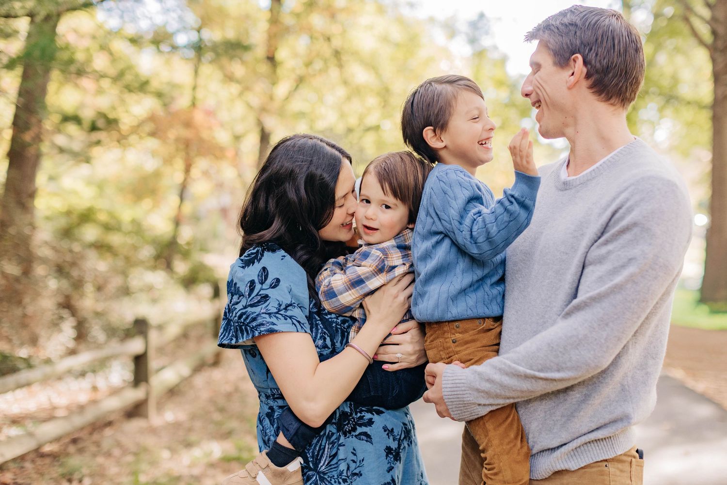 A joyful outdoor family photoshoot with casual attire against a wooded backdrop.
