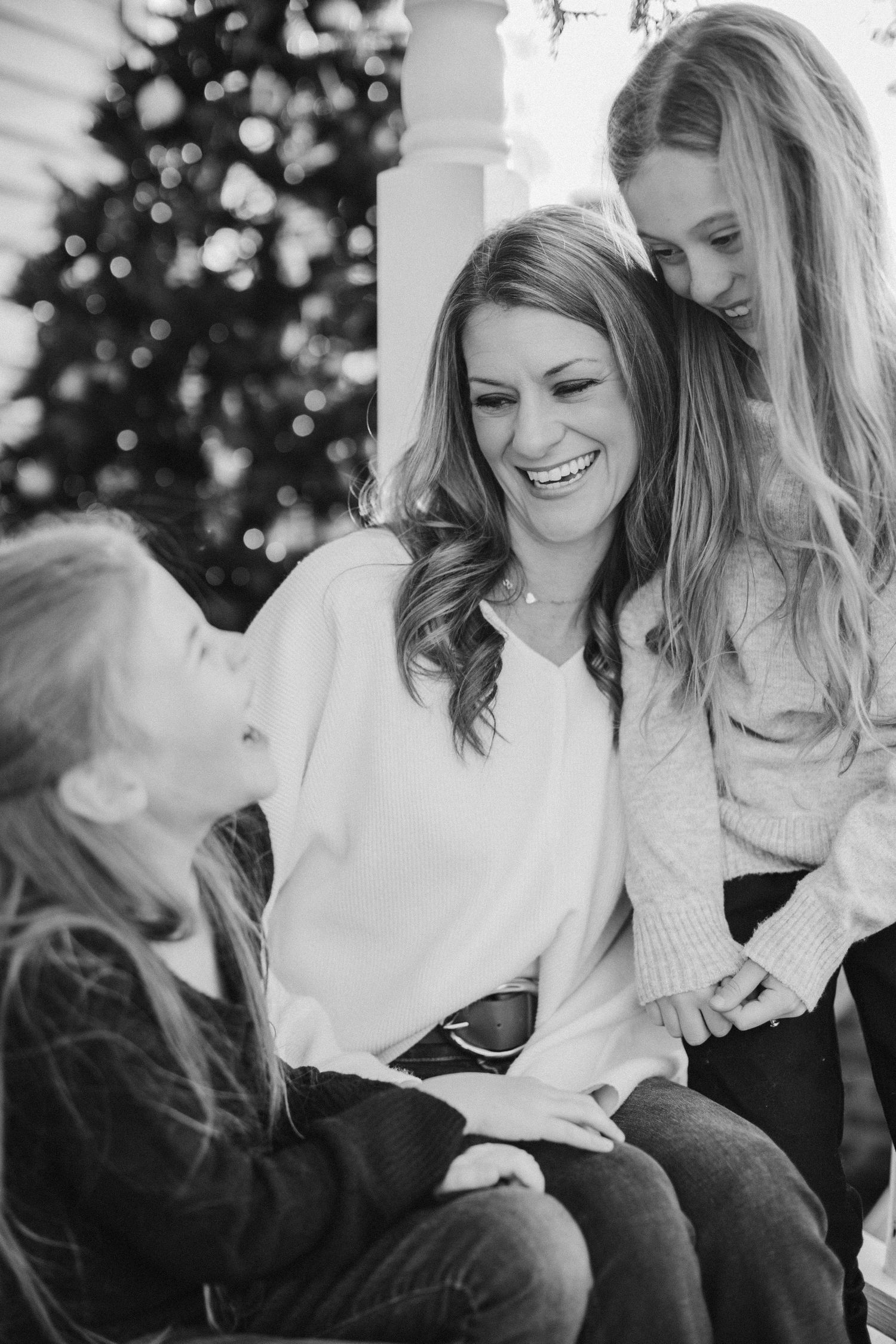 Candid black and white photo of people laughing together by a Christmas tree.